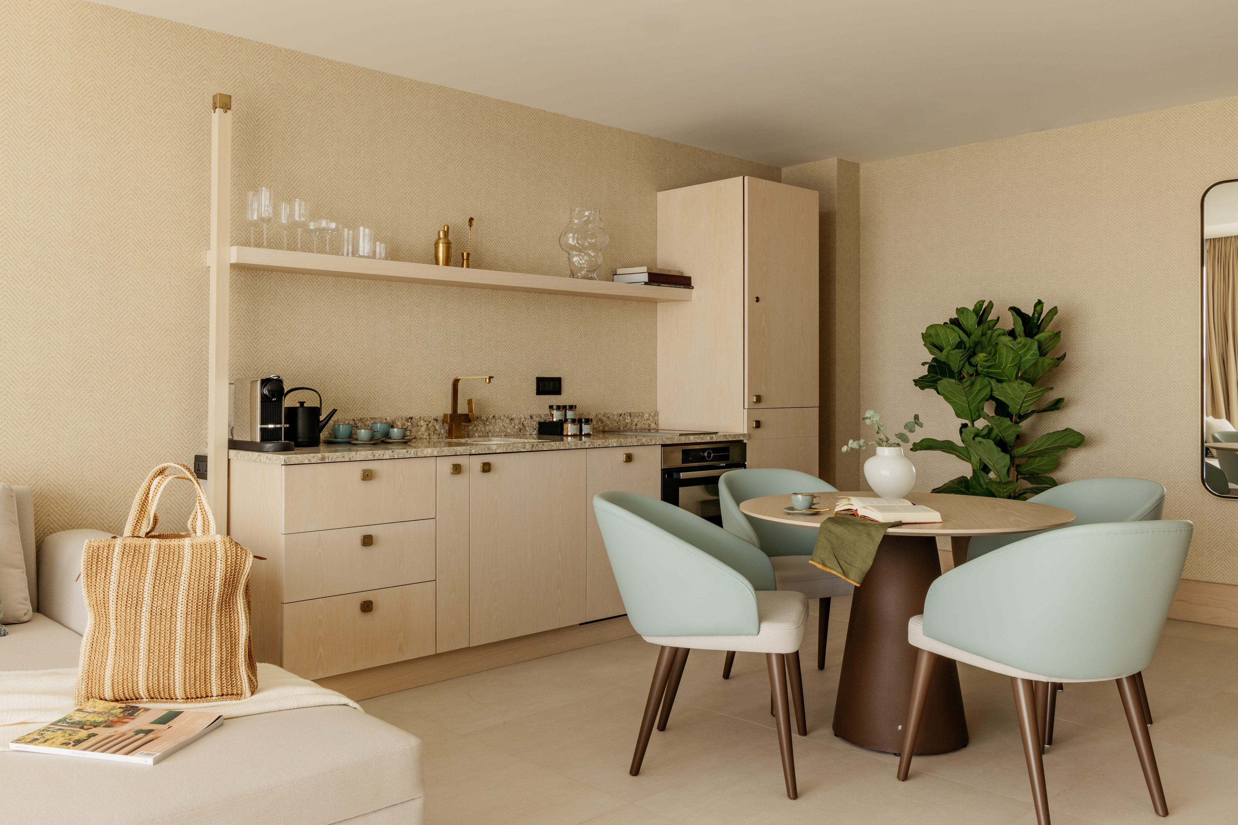 Modern apartment kitchenette, dining area with light wood and blue chairs.