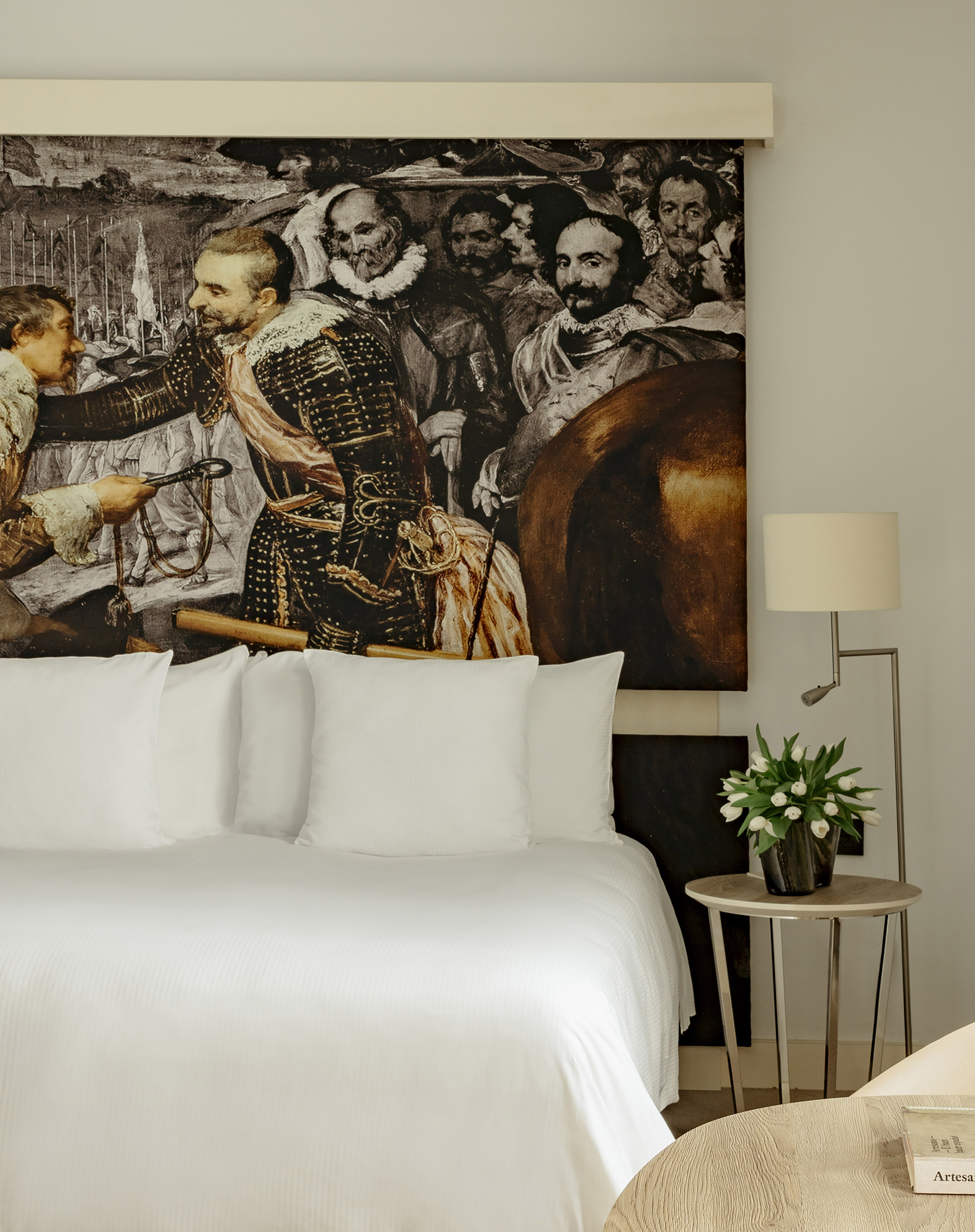Modern hotel bedroom with white bed, historical art mural, and fresh tulips.