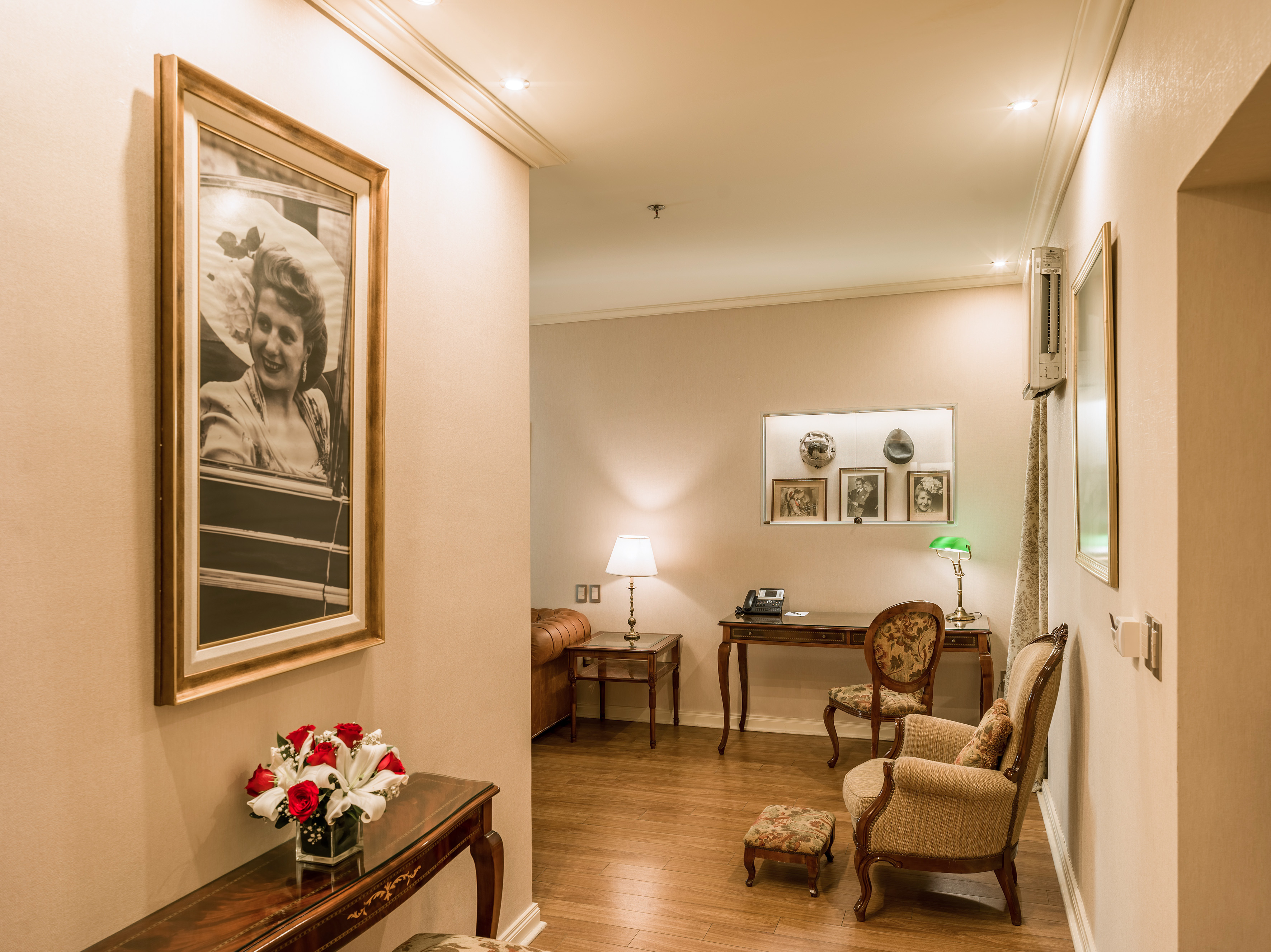 Luxurious hotel suite with vintage portrait, flowers, and traditional desk area.