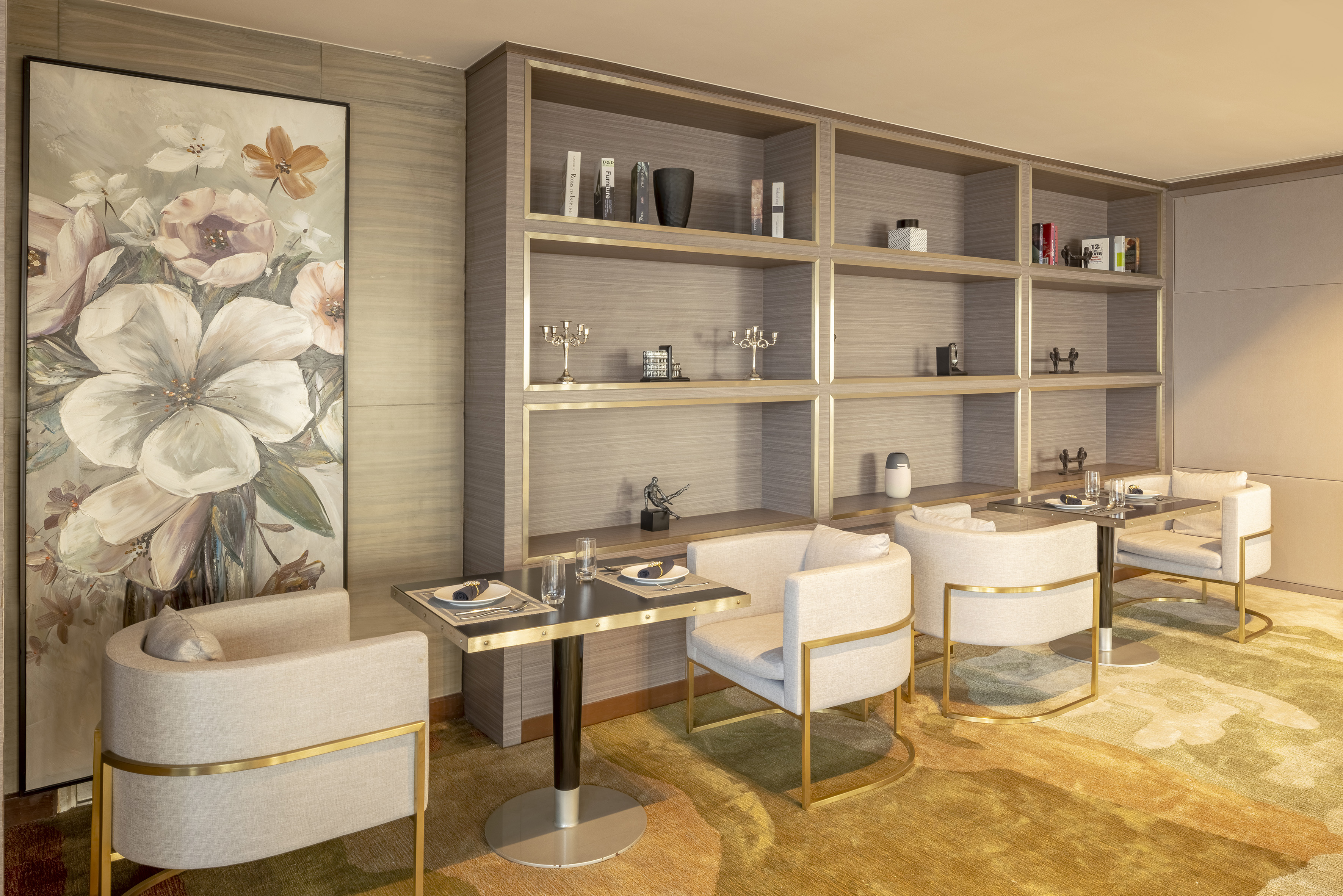 Elegant modern lounge with gold-framed chairs, wooden shelving, and floral wall art.