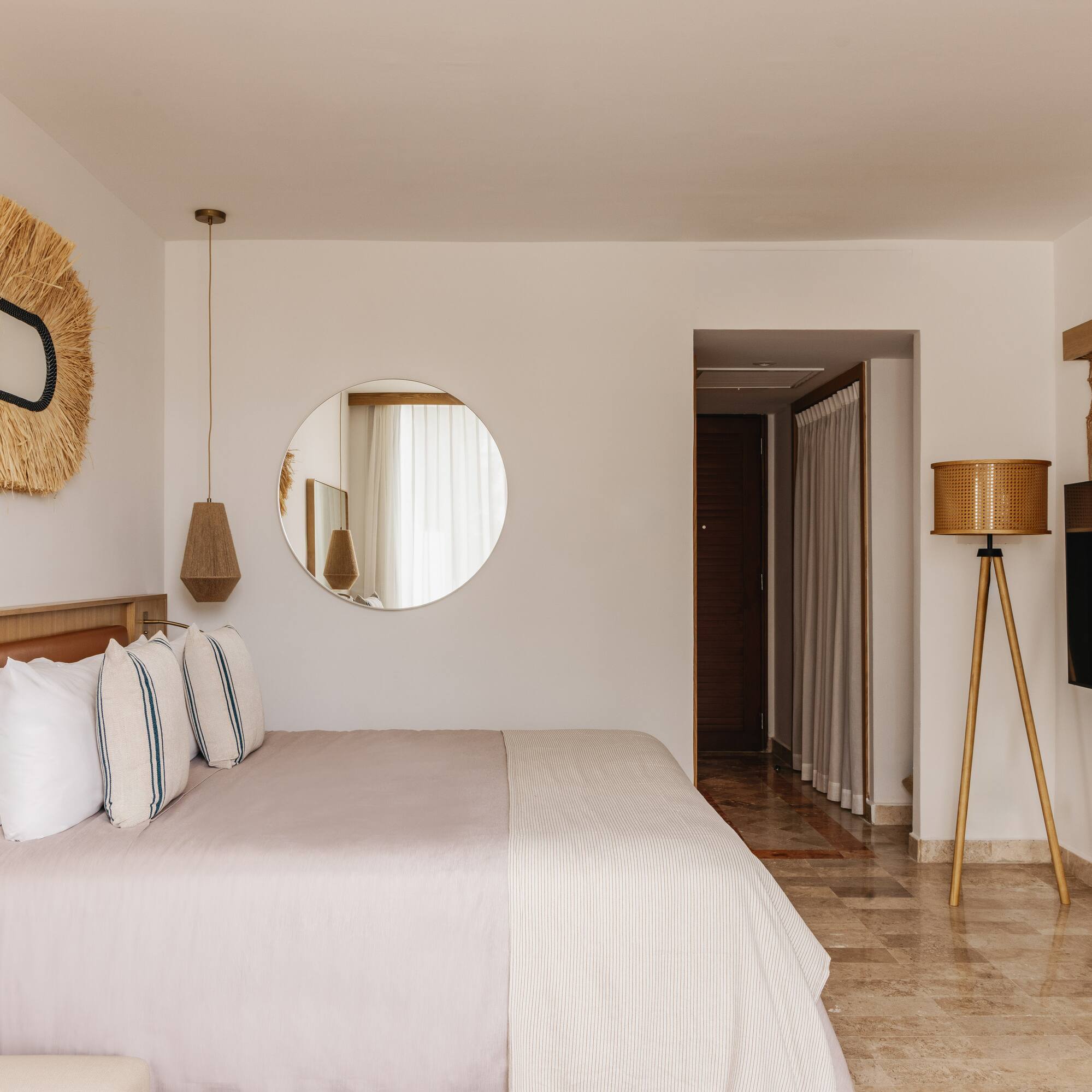 Modern hotel bedroom with large bed, natural decor, round mirror, and TV.