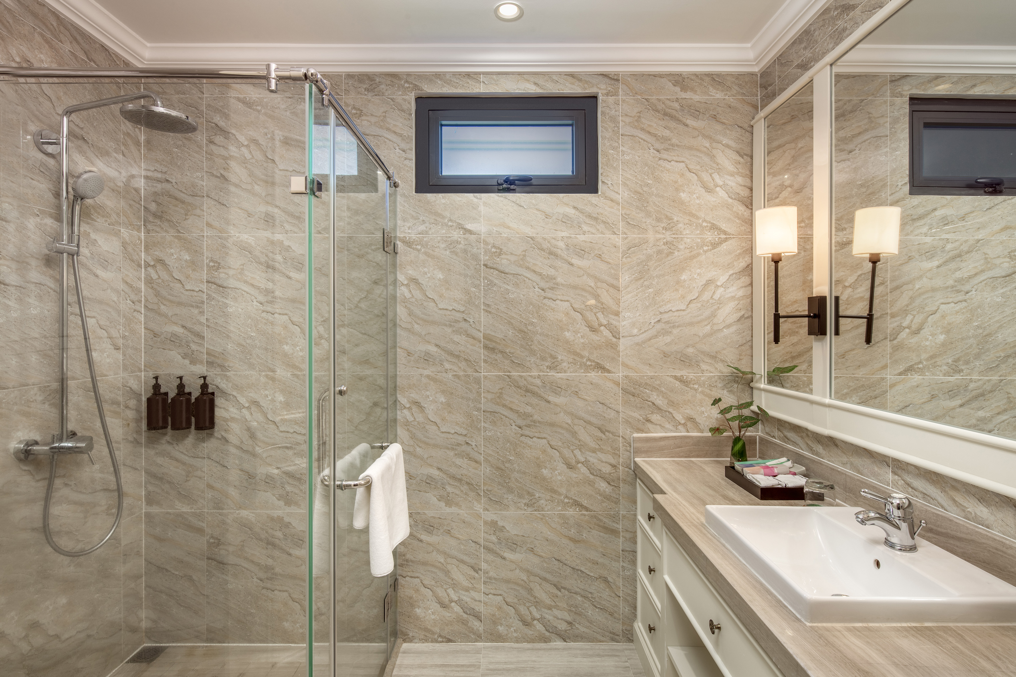 Hotel bathroom featuring walk-in glass shower, vanity with sink, and marble tiled walls.