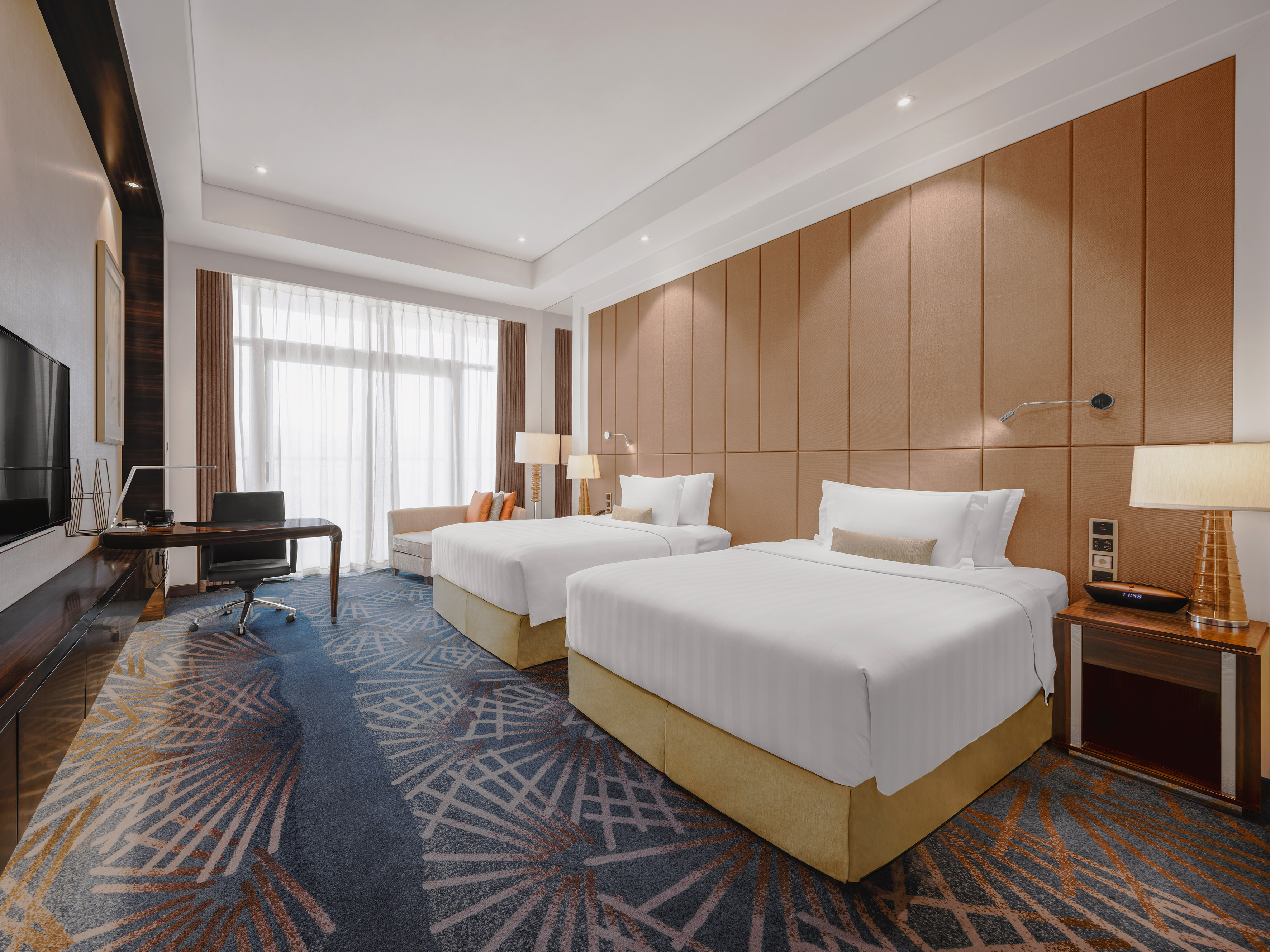 Modern hotel room with two twin beds, work desk, and large window.