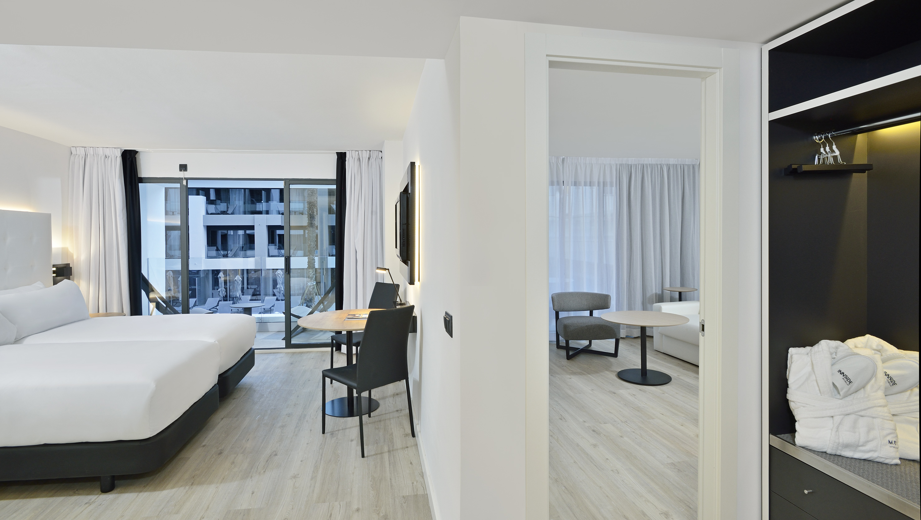 Modern hotel suite with two beds, balcony access, dining, and lounge area.