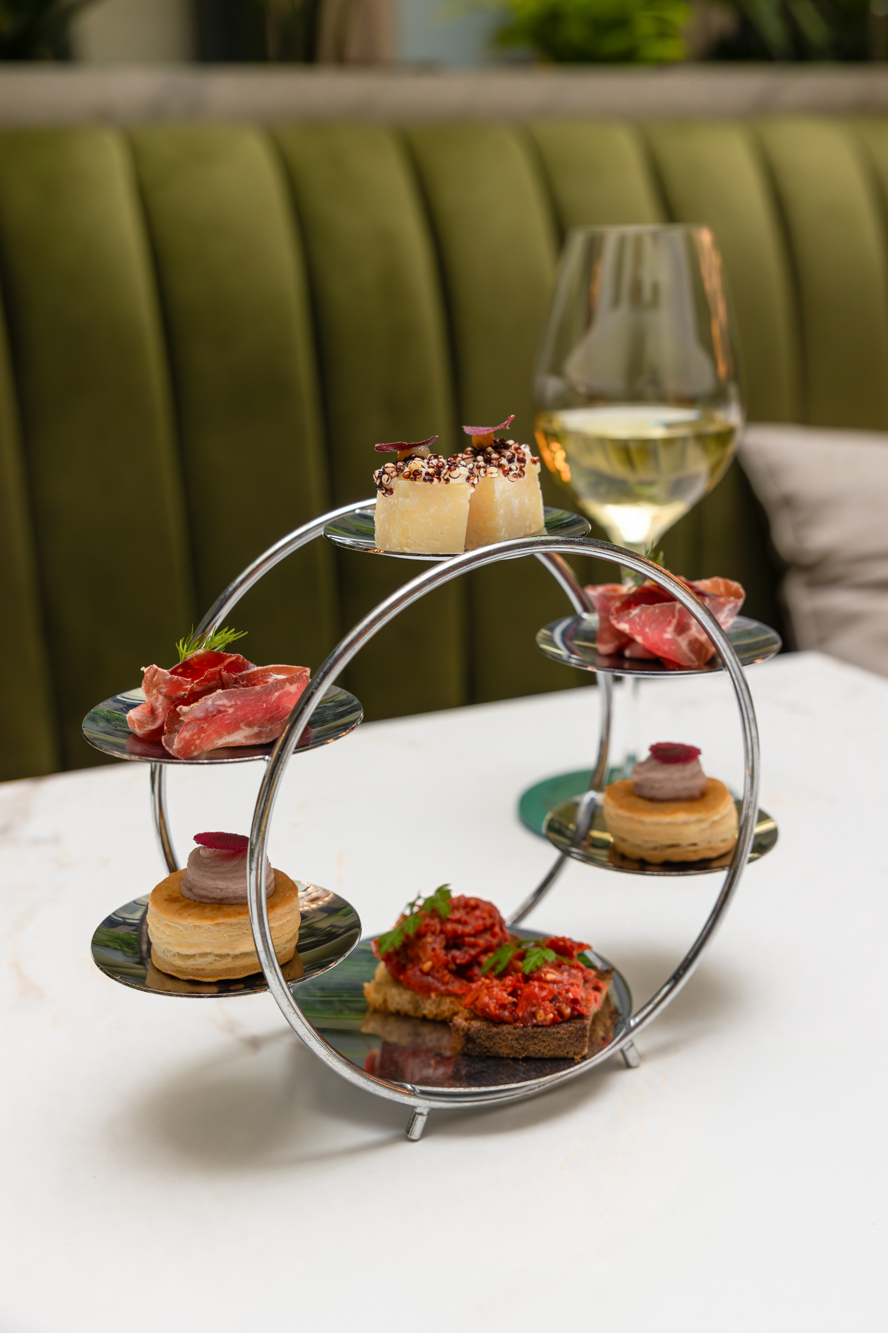 Assorted gourmet appetizers on a unique silver stand with white wine.