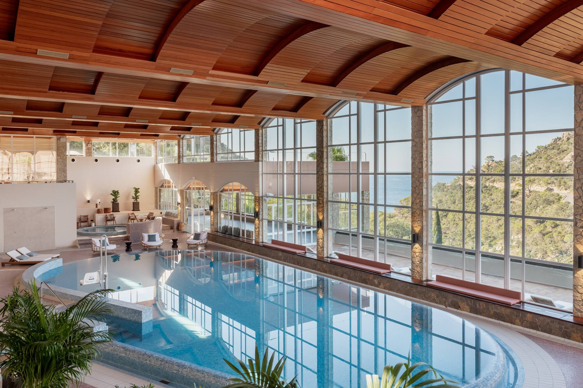 Luxury indoor spa pool with ocean view, large windows, wood ceiling.