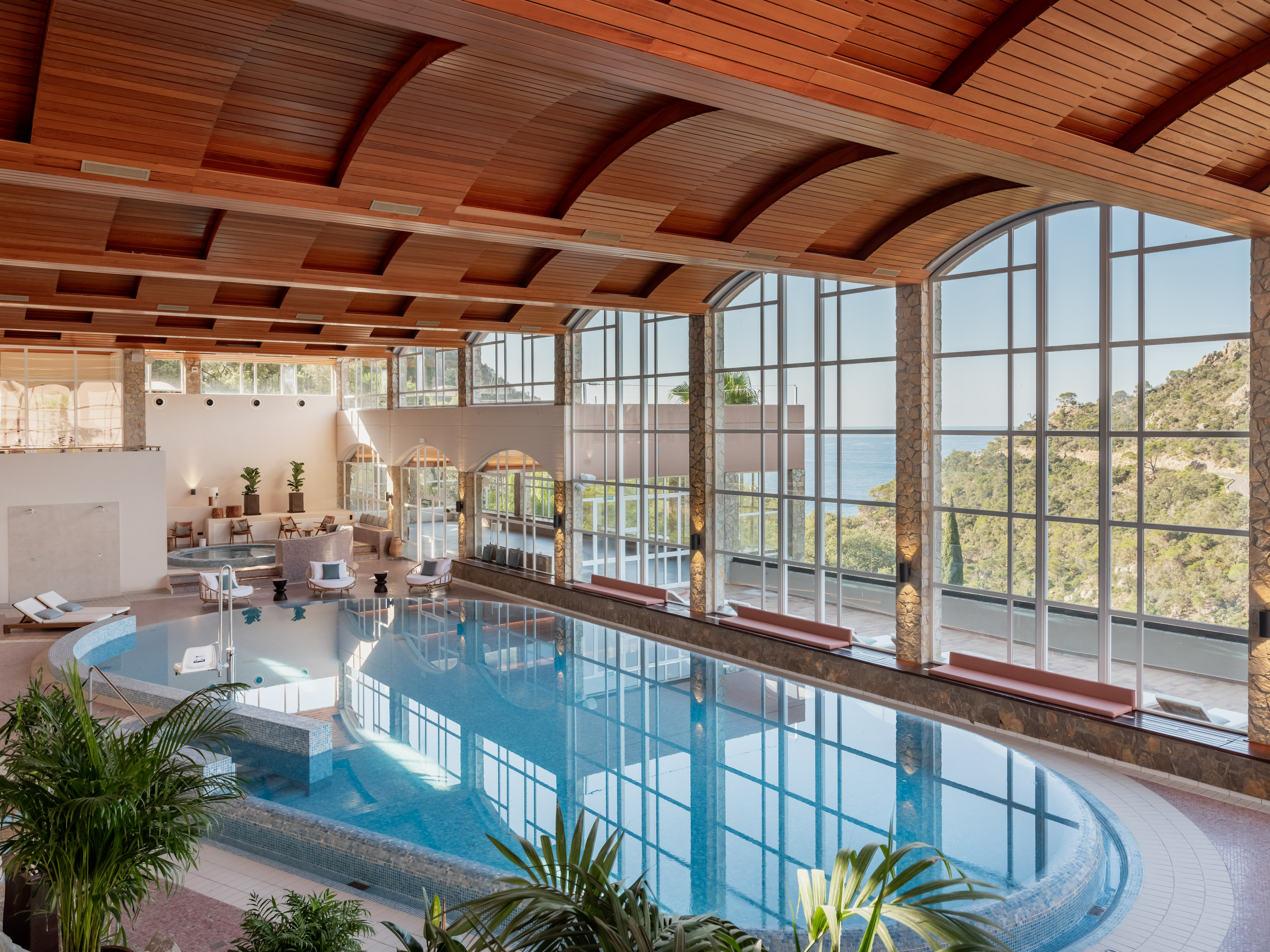 Luxury indoor spa pool with ocean view, large windows, wood ceiling.