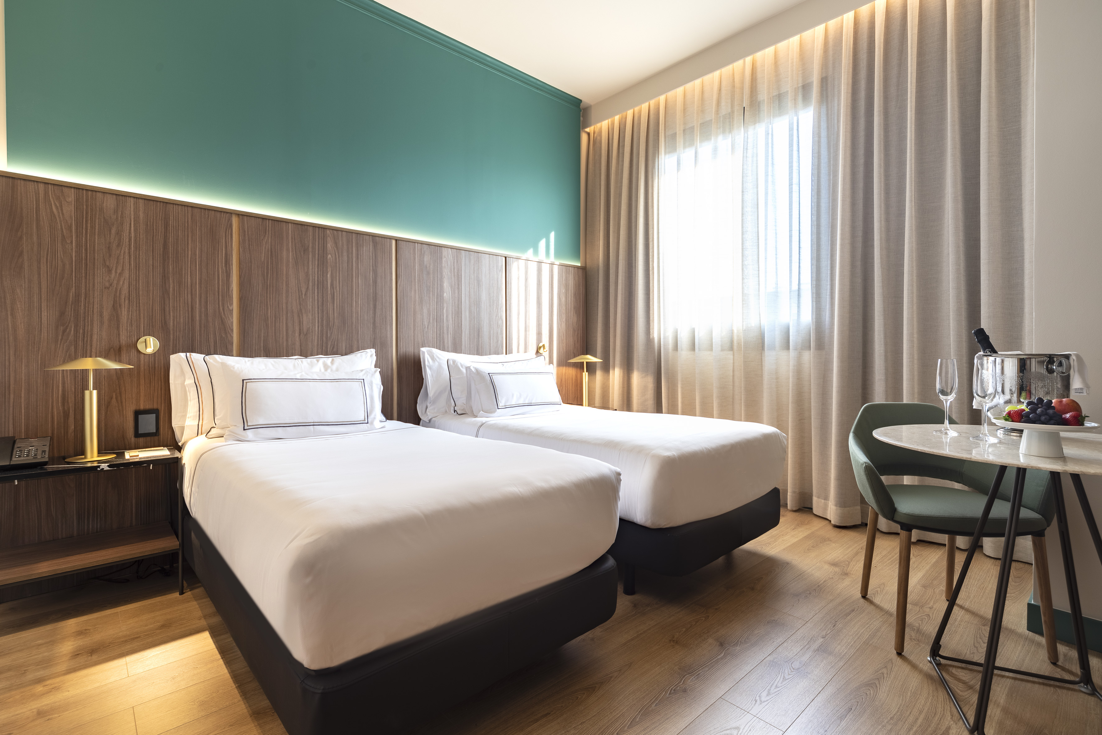 Modern hotel room, two twin beds, teal accent wall, and champagne setup.
