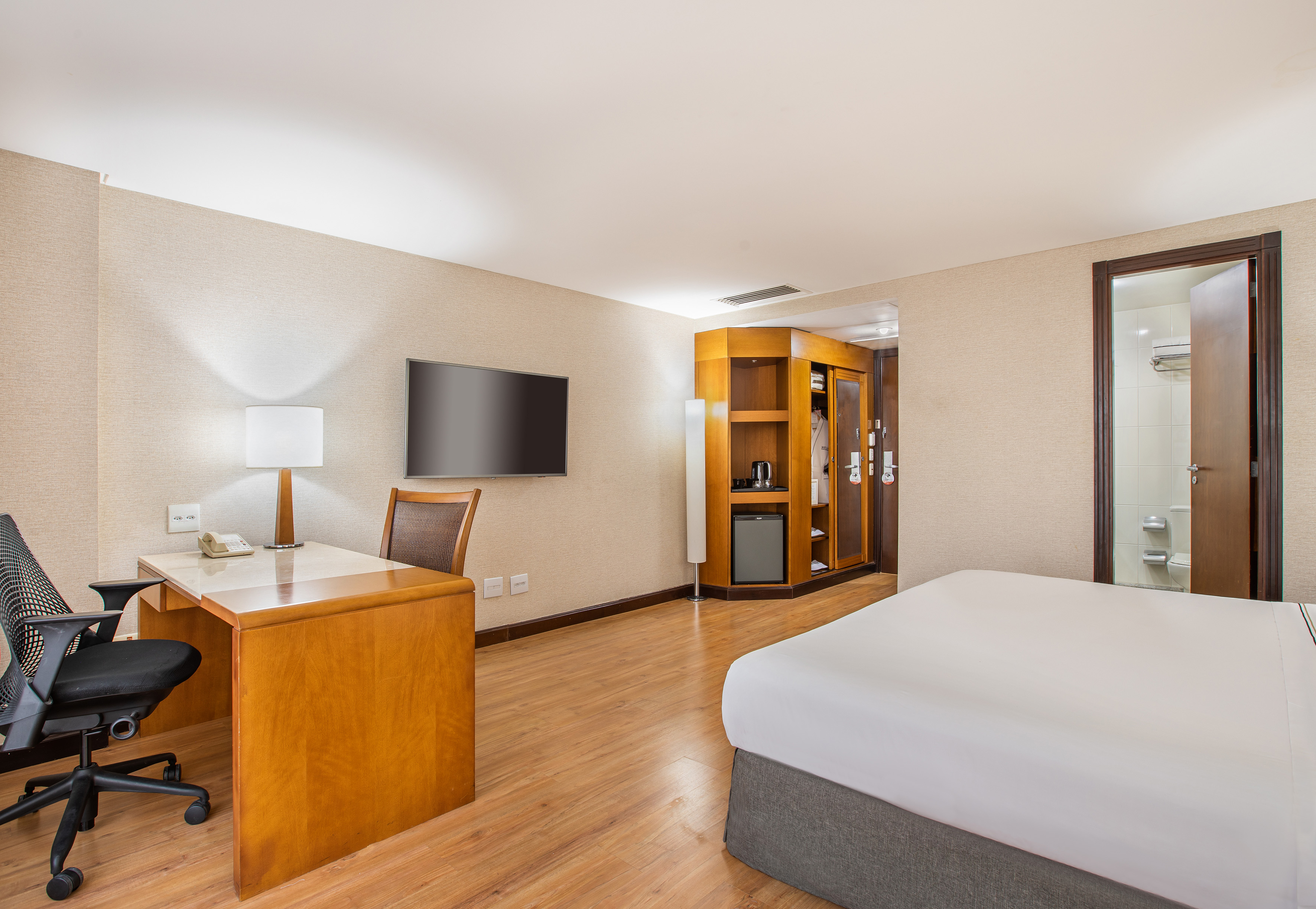 Modern hotel room with bed, desk, TV, minibar, and a glimpse of the bathroom.