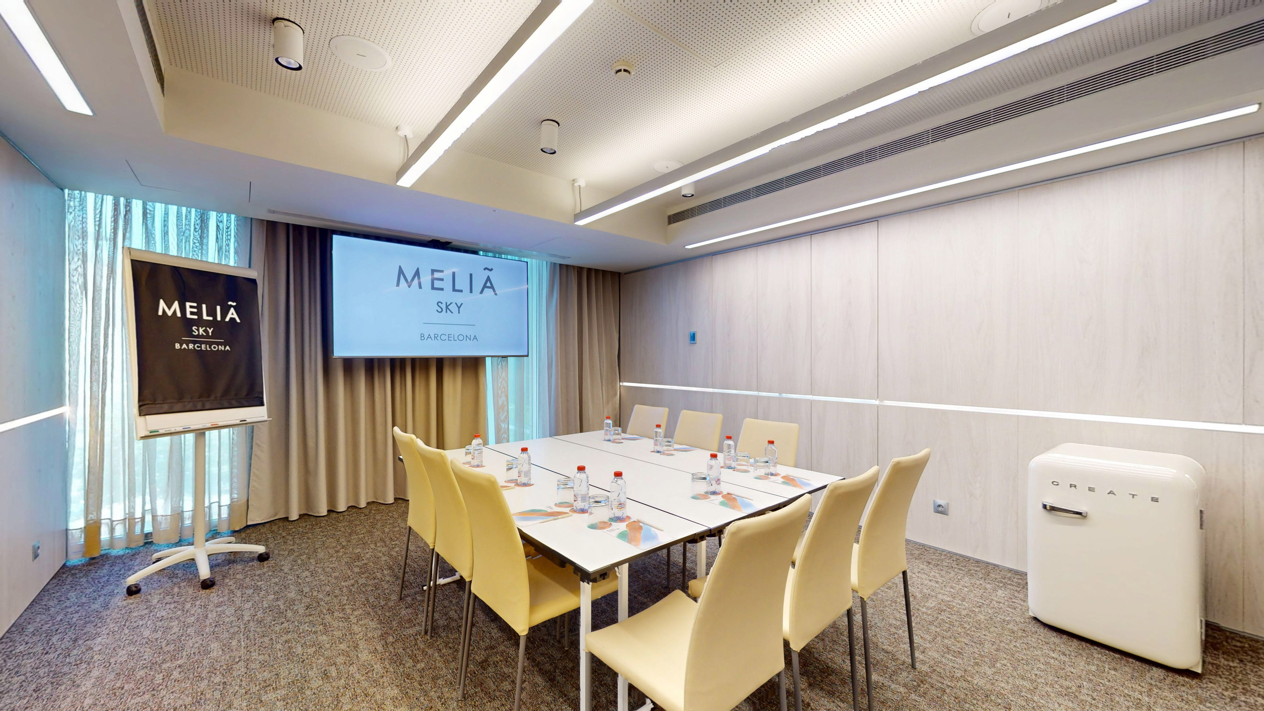Melia Sky Barcelona modern meeting room with screen, conference table, chairs.