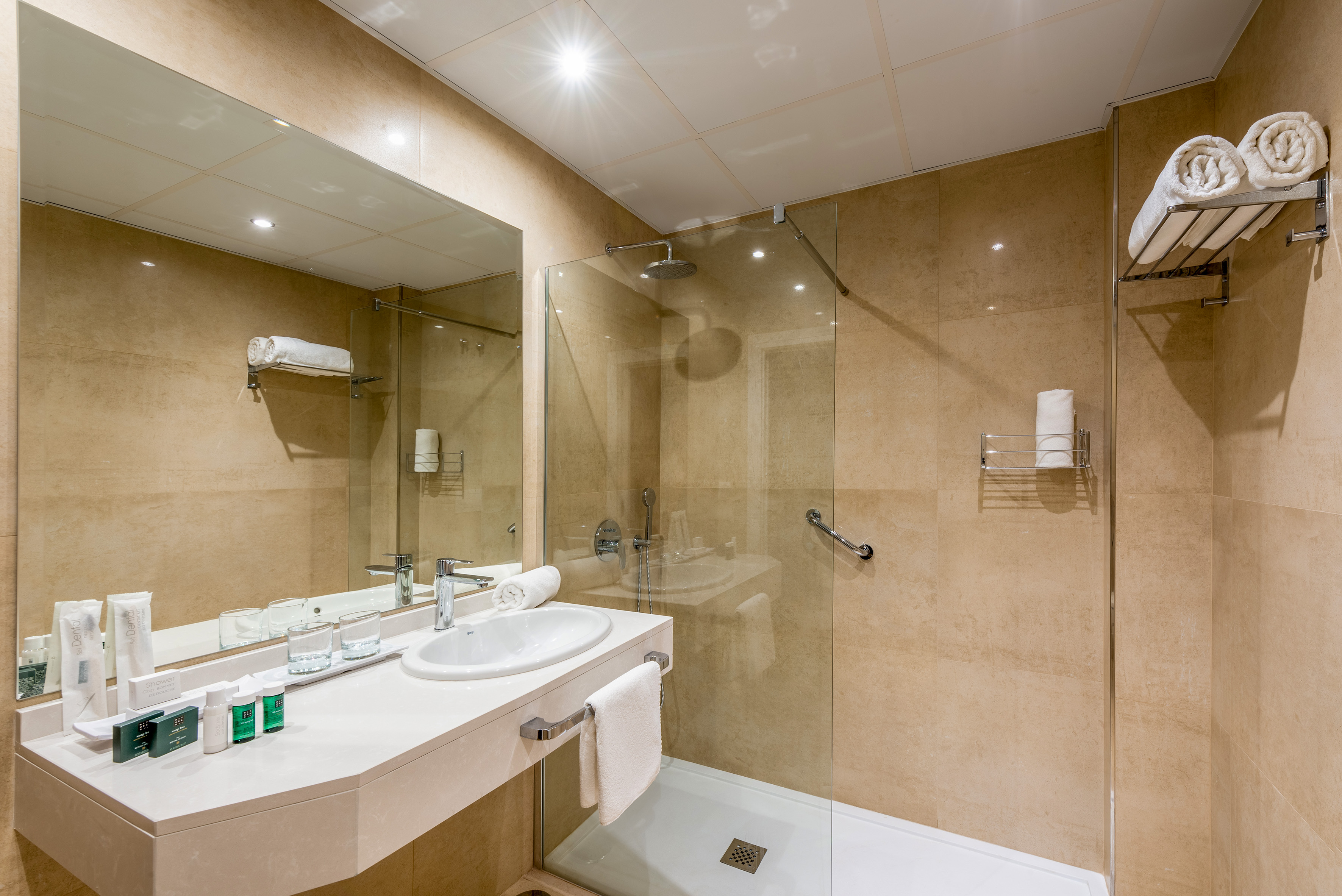 Modern hotel bathroom with walk-in shower, vanity, mirror, and amenities.