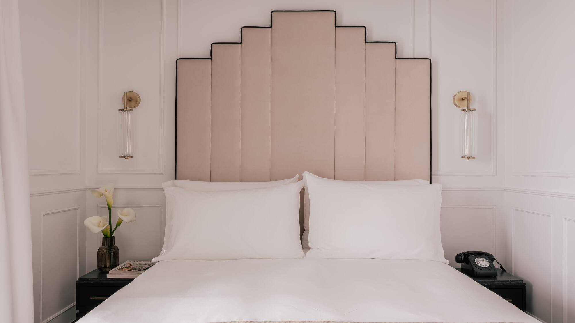 Luxury hotel bed with pink Art Deco headboard, white bedding, vintage phone.