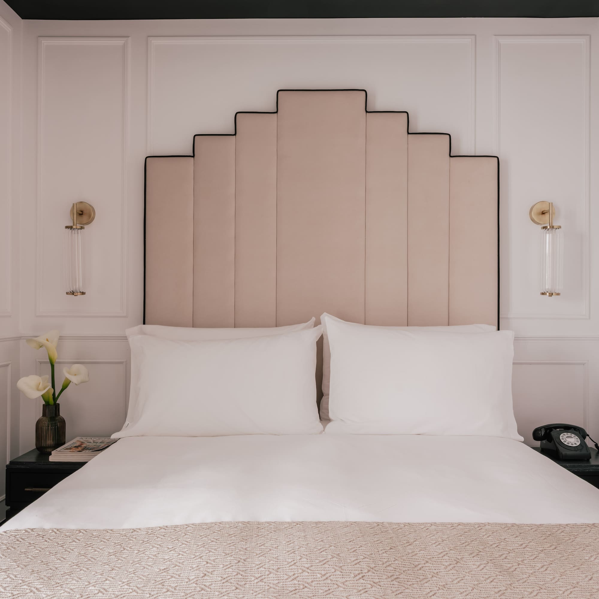 Boutique hotel bedroom with Art Deco headboard, white bed, nightstands.