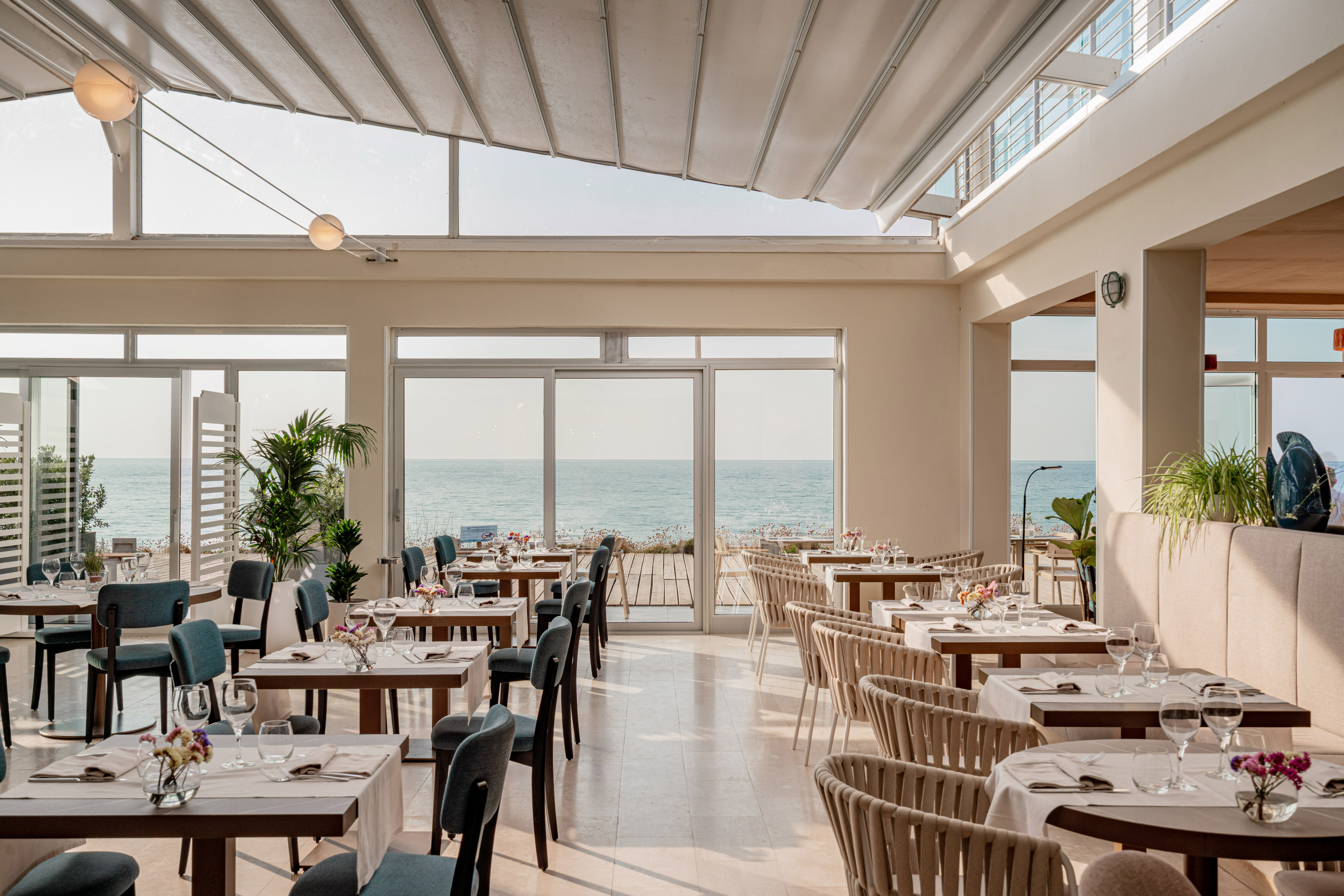 Bright oceanfront restaurant with dining tables, large windows, and sea views.