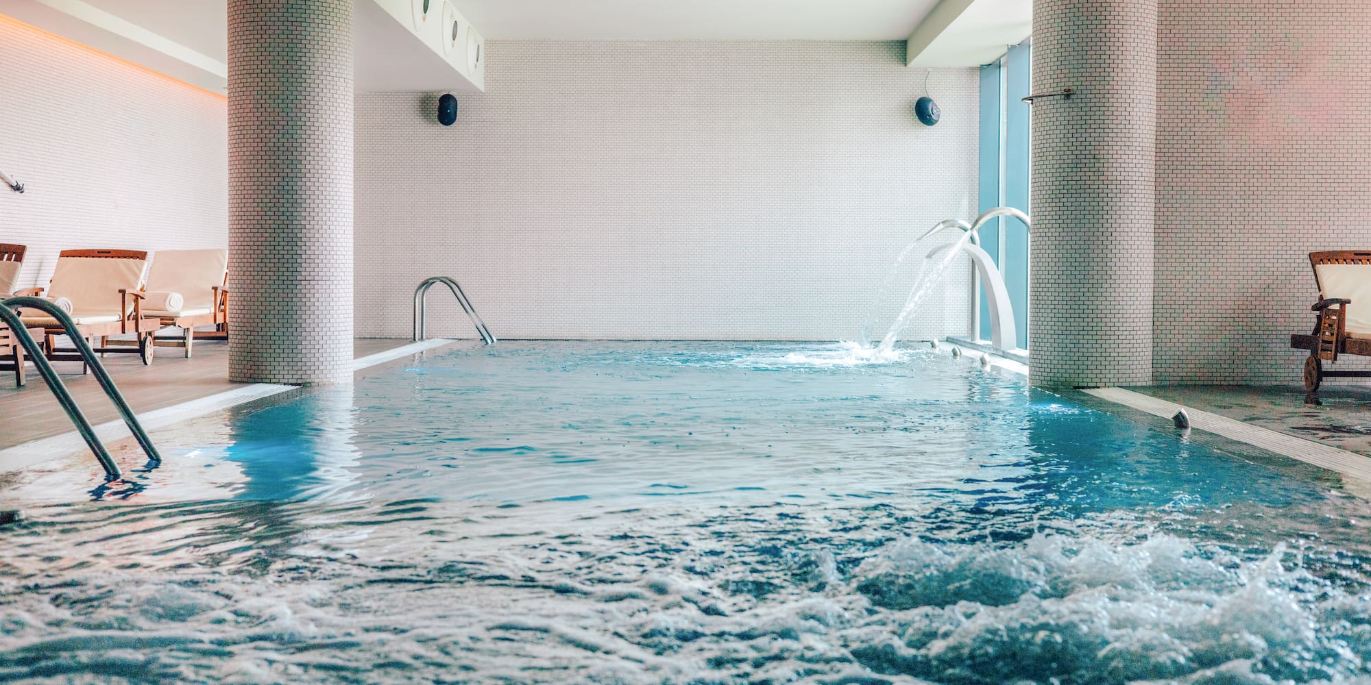 Indoor spa pool with bubbling water features and poolside loungers.