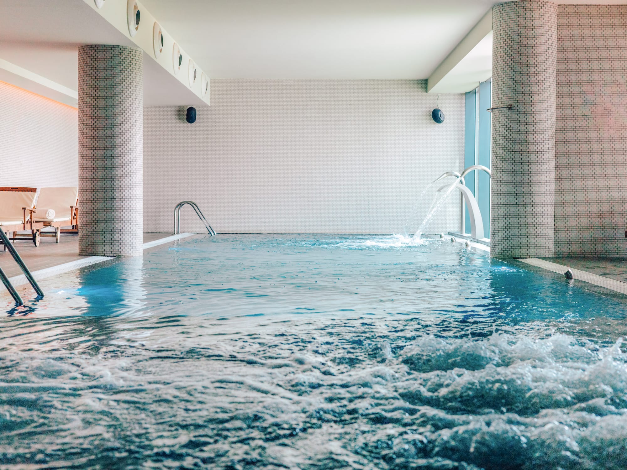Indoor pool with bubbling spa jets, water features, and white tiled walls.