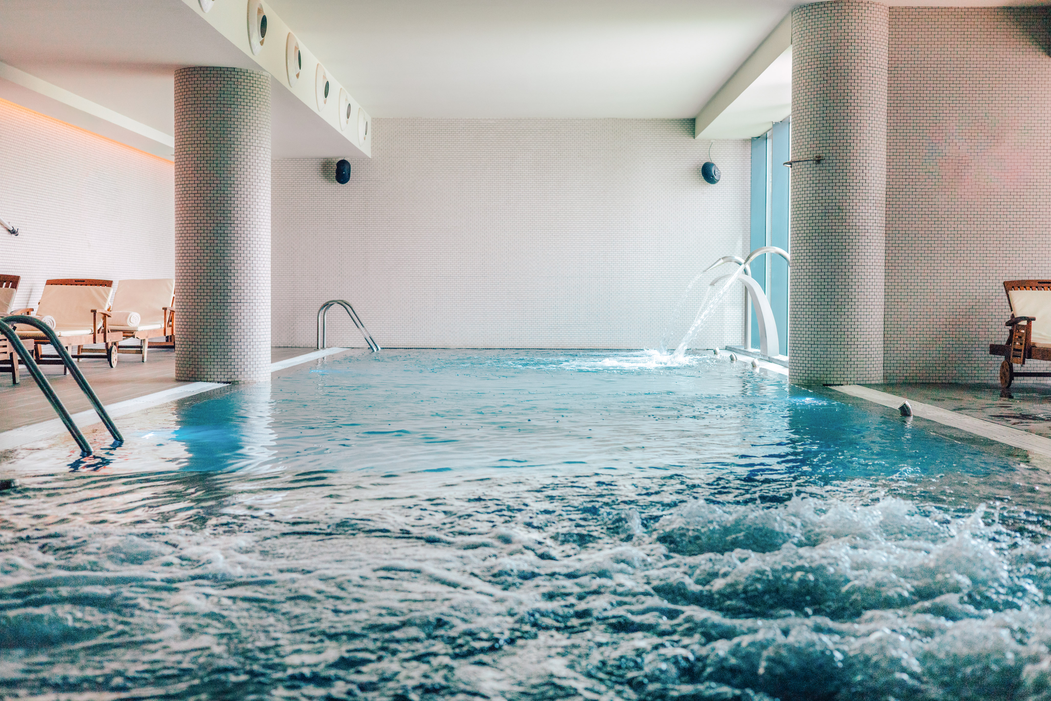 Indoor pool with bubbling water, decorative fountains, and lounge chairs.