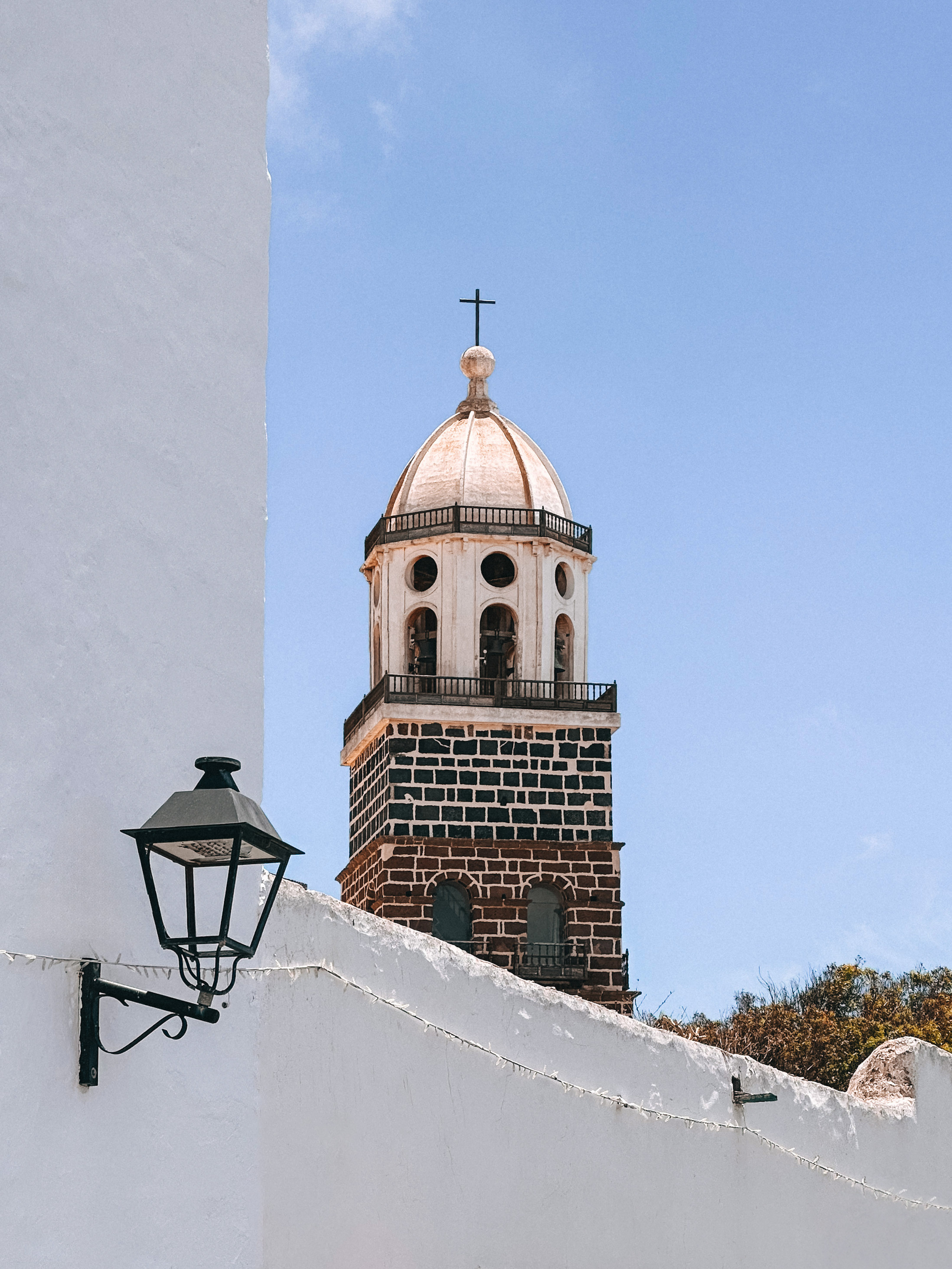 Church bell tower with white dome, cross, and dark brick base against blue sky.