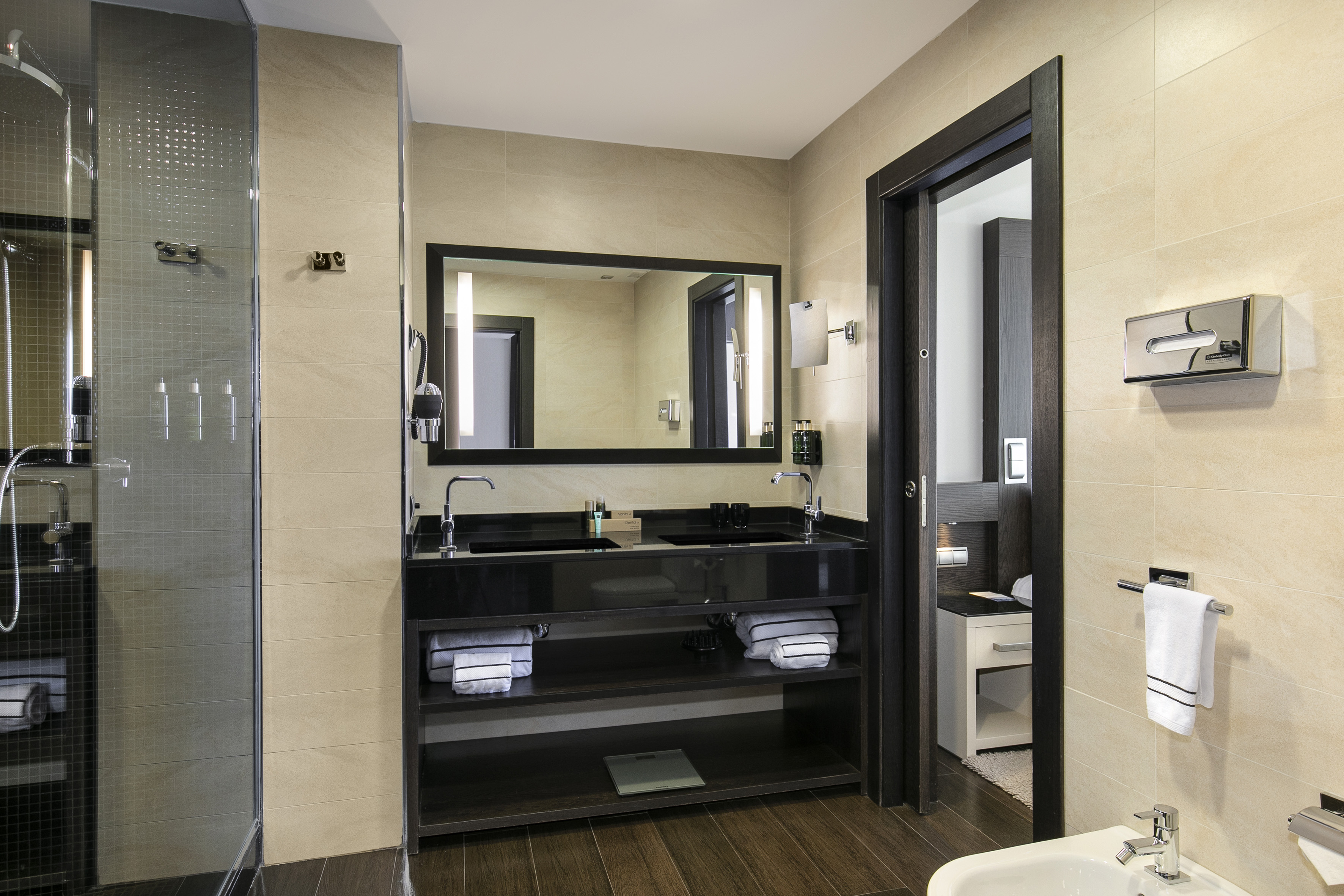 Modern hotel bathroom with double vanity, large mirror, and glass shower.