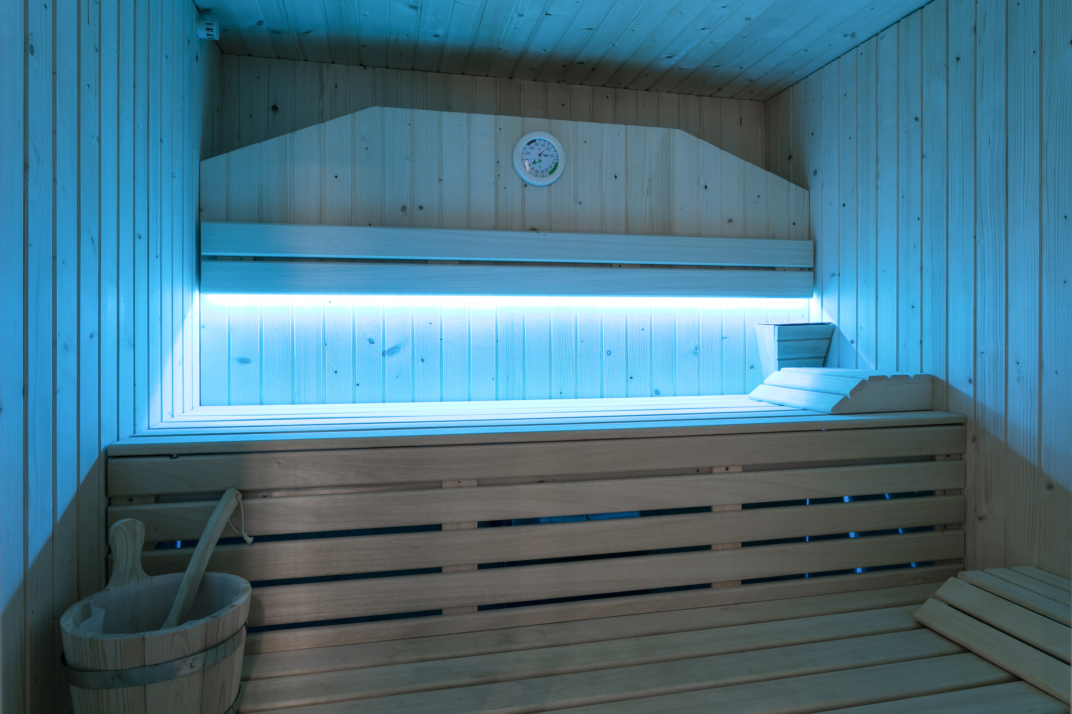 Wooden sauna interior with blue LED lighting, benches, thermometer, and bucket.