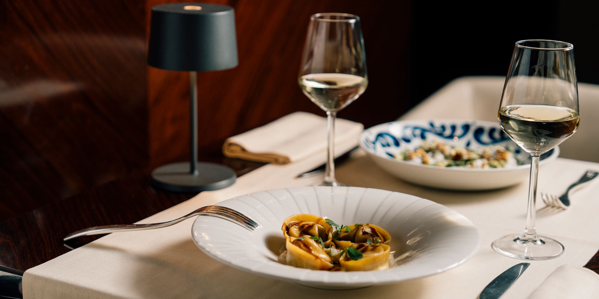 Tortellini pasta dish with white wine glasses on elegant restaurant table.