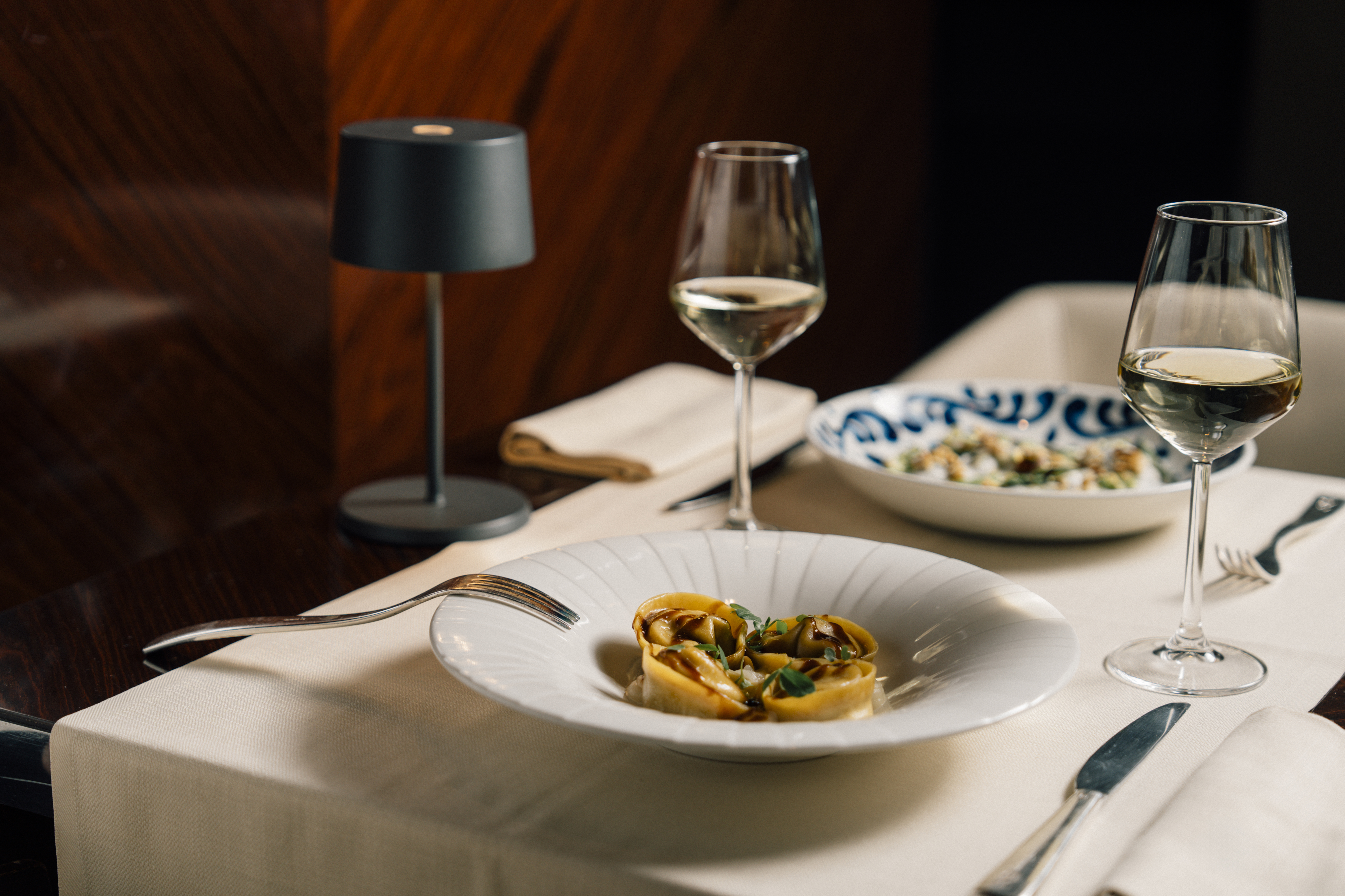 Tortellini pasta dish with white wine glasses on elegant restaurant table.