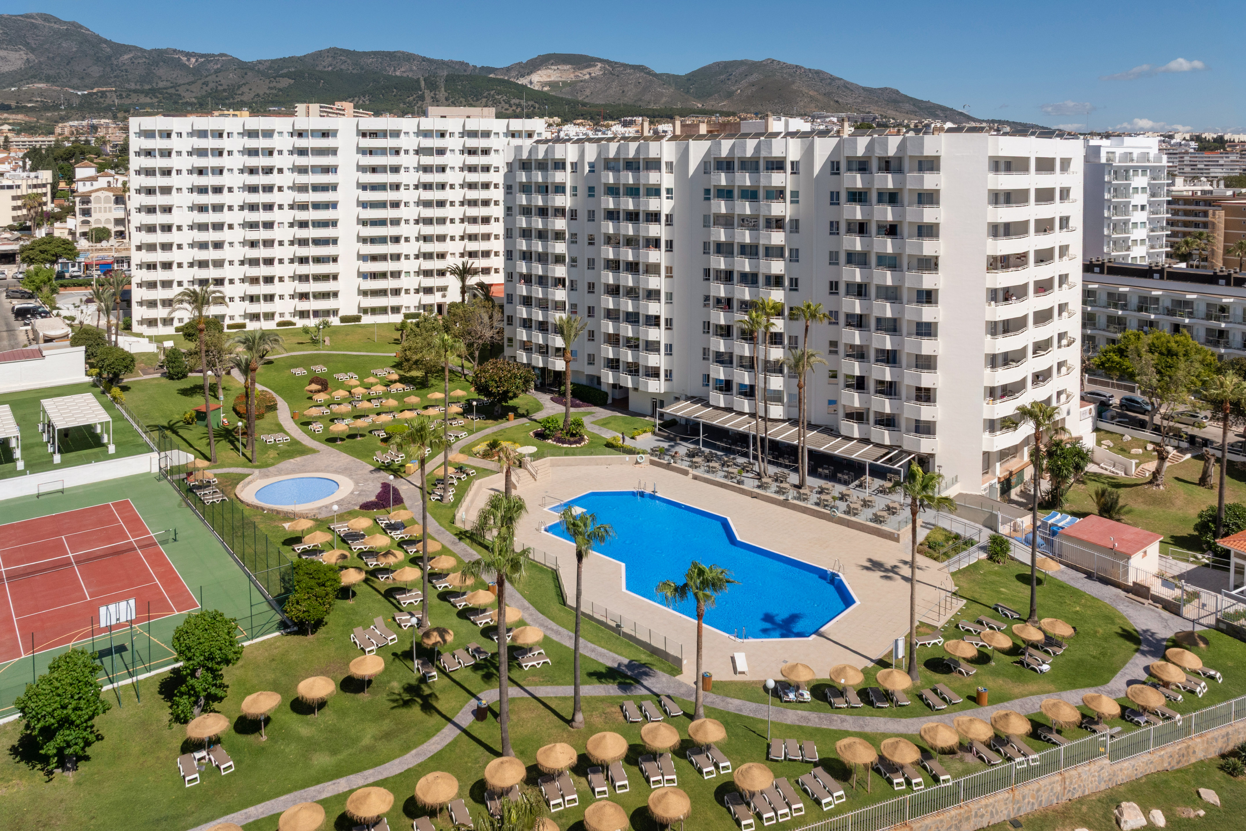 Hotel resort with pools, tennis court, palm trees, and white apartment buildings.