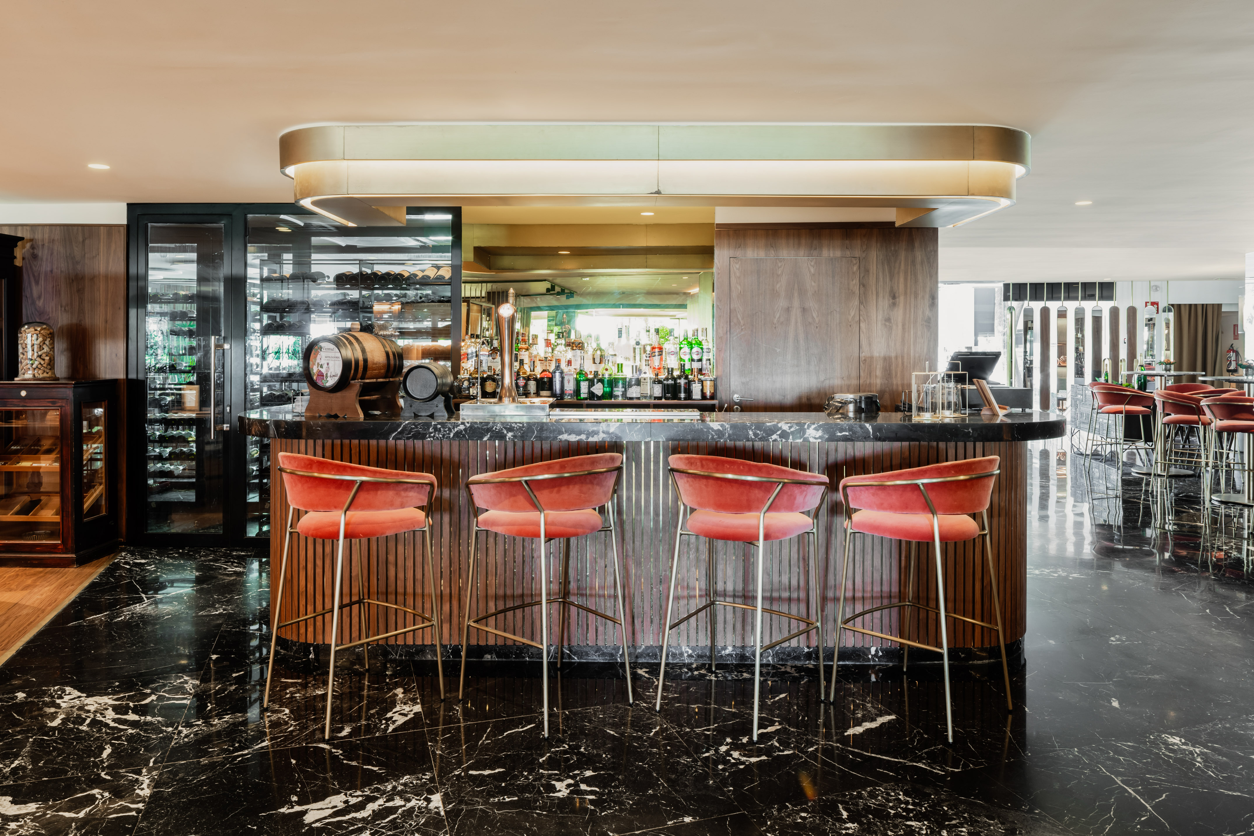 Elegant bar with black marble counter, red velvet stools, and wine display.