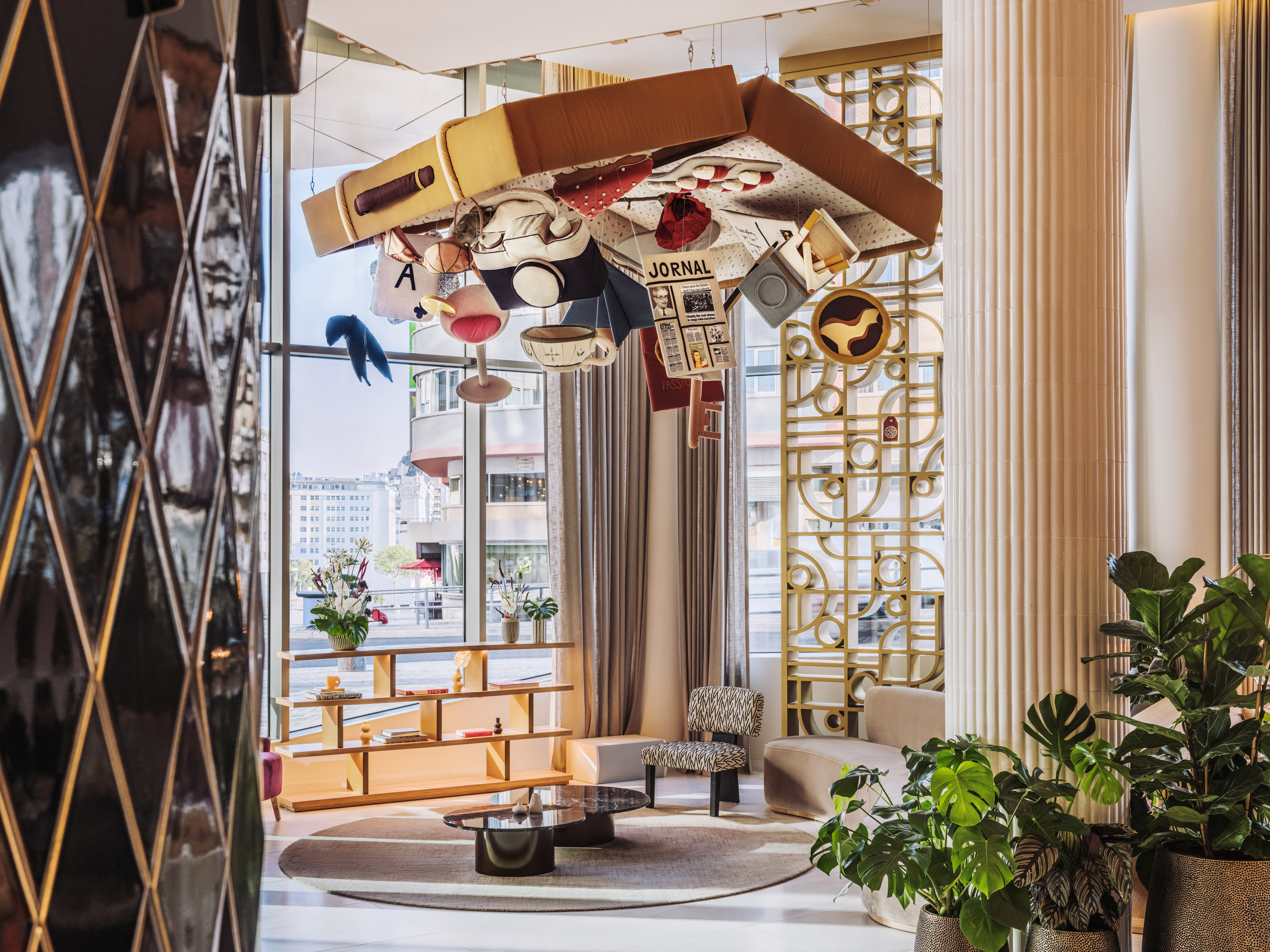 Modern hotel lobby with unique suspended suitcase art, stylish furniture, and plants.