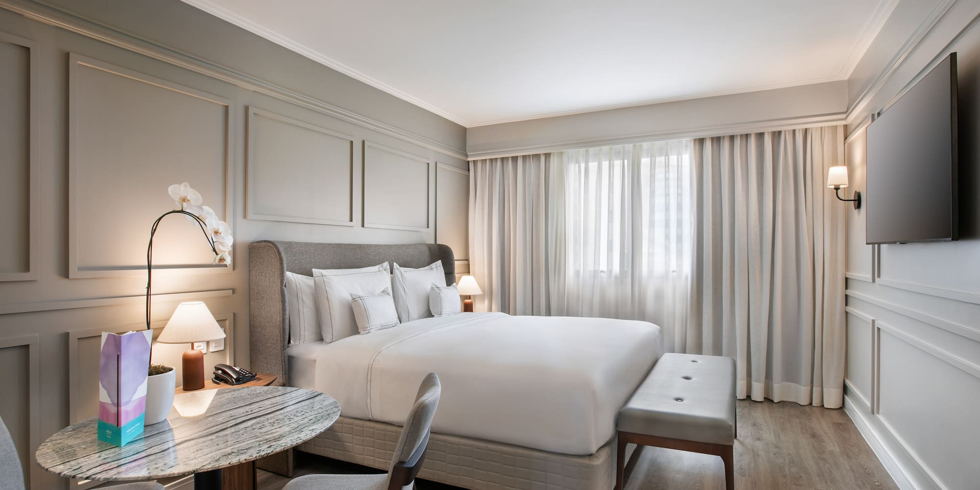 Modern hotel bedroom with comfortable king bed, grey decor, and sitting area.