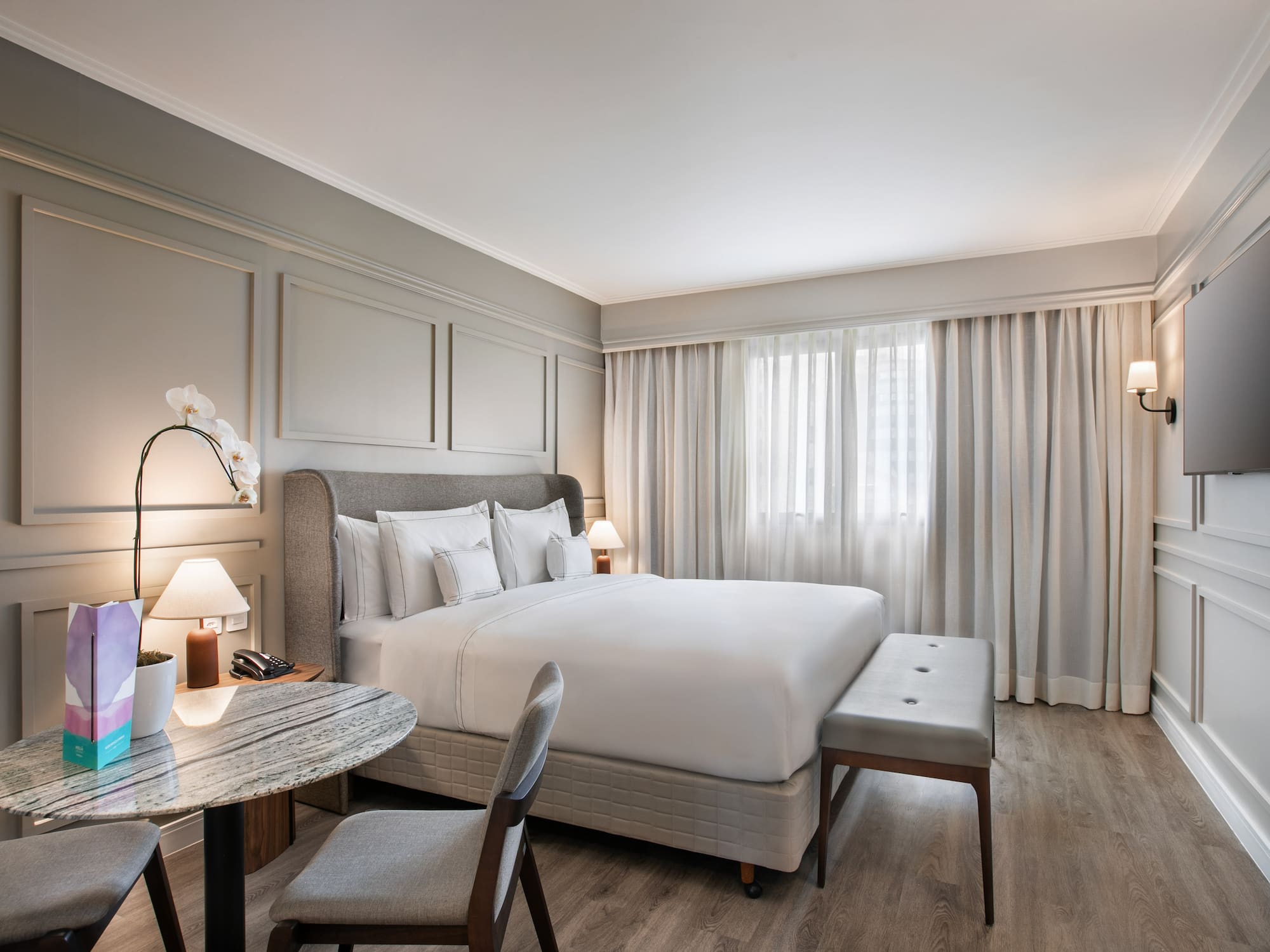Modern hotel bedroom with comfortable king bed, grey decor, and sitting area.
