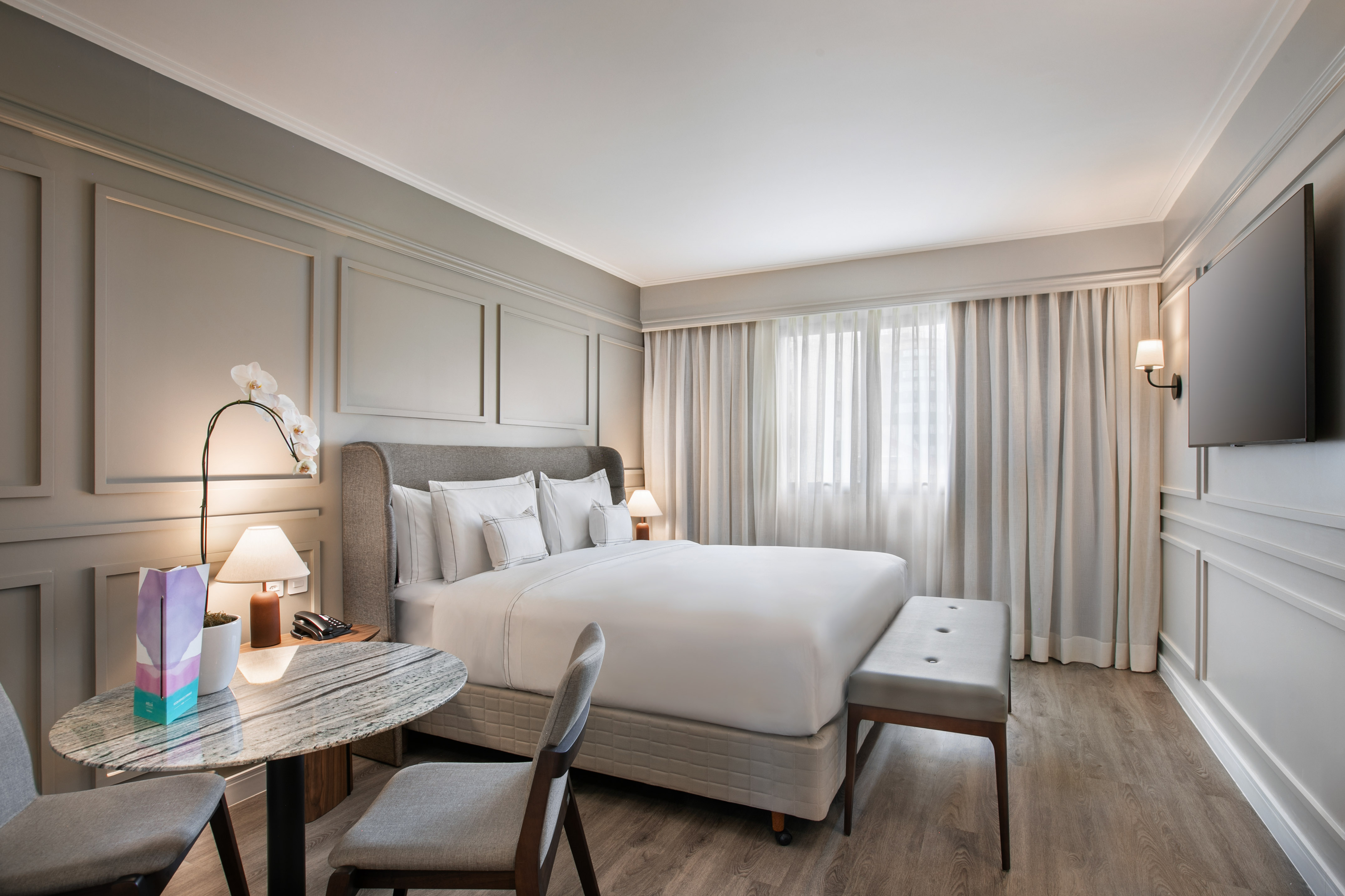Modern hotel bedroom with comfortable king bed, grey decor, and sitting area.