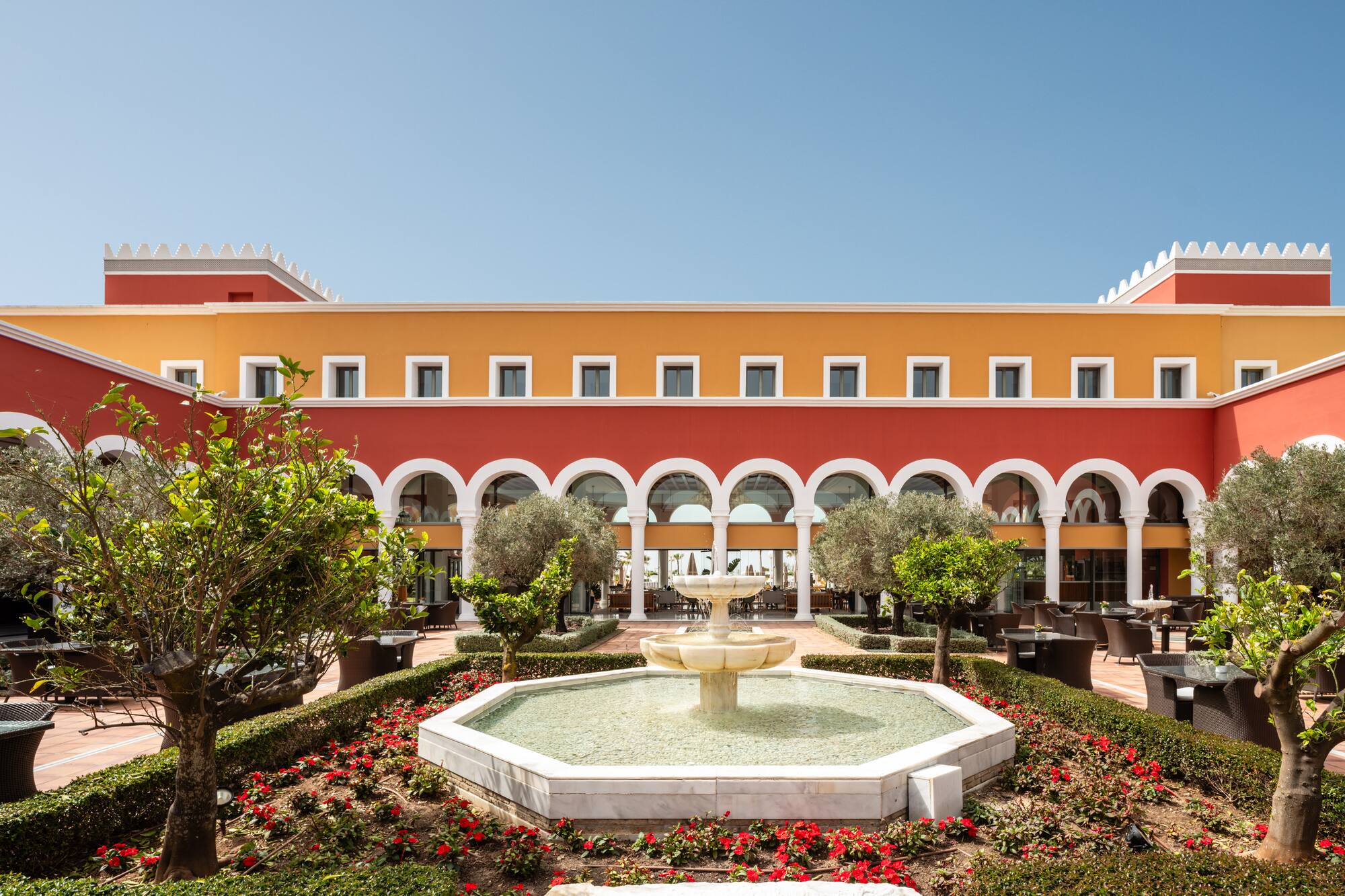 Red and orange hotel courtyard with arches, central fountain, and lush garden.
