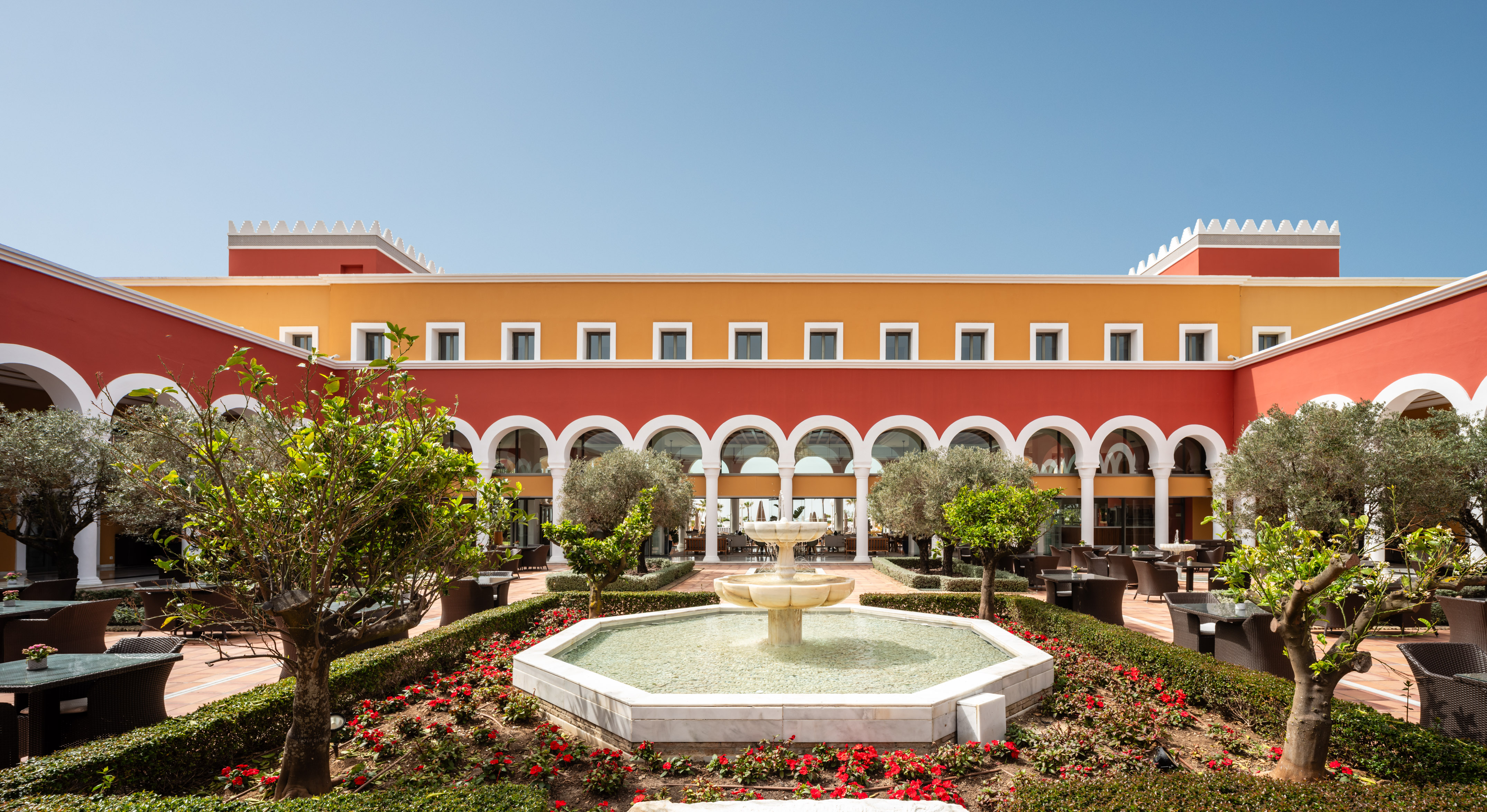 Red and orange hotel courtyard with arches, central fountain, and lush garden.
