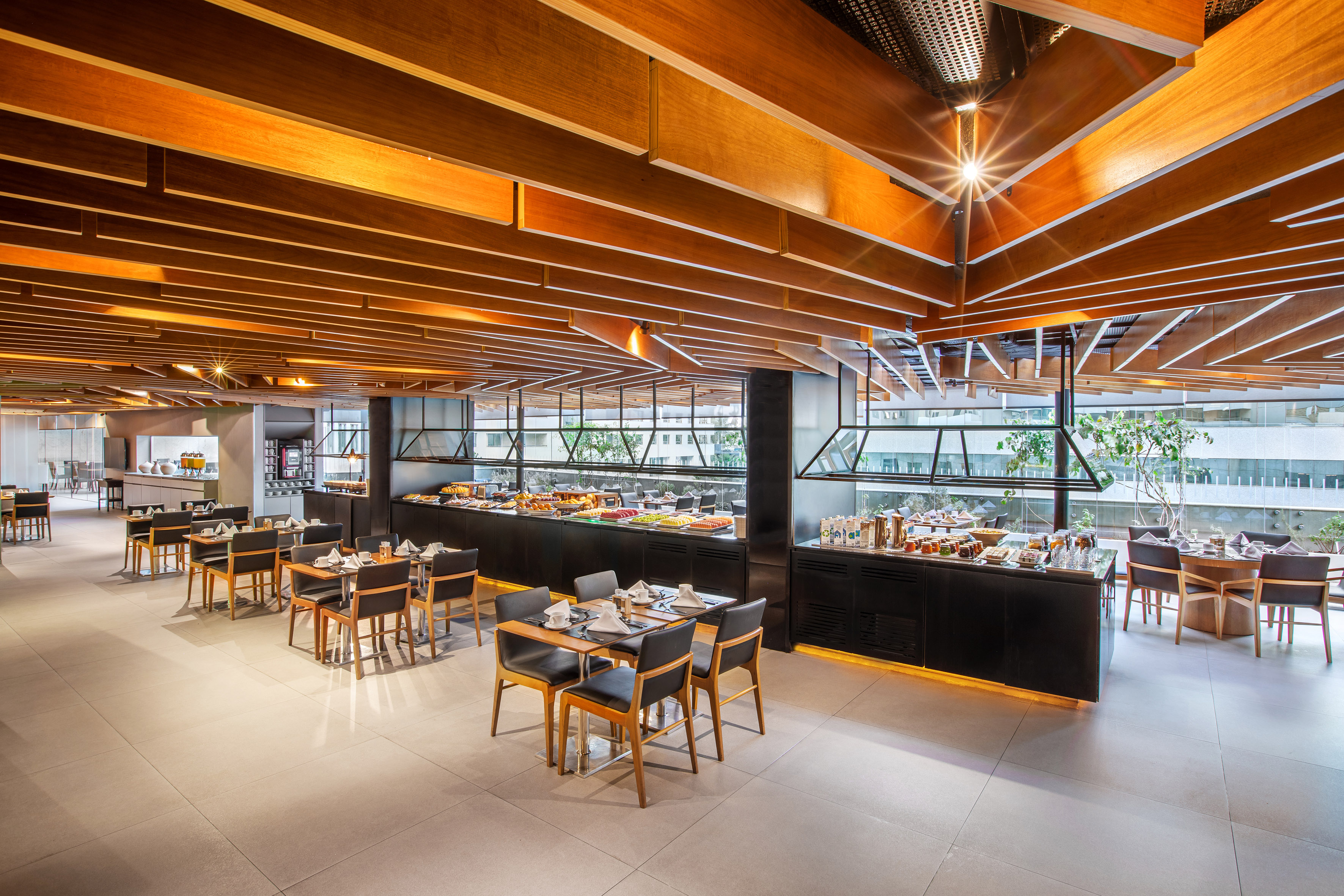 Modern hotel restaurant buffet with food, dining tables, and wood ceiling.