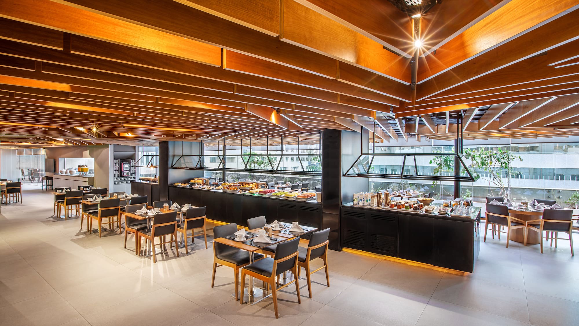 Modern hotel restaurant buffet with food, dining tables, and wood ceiling.
