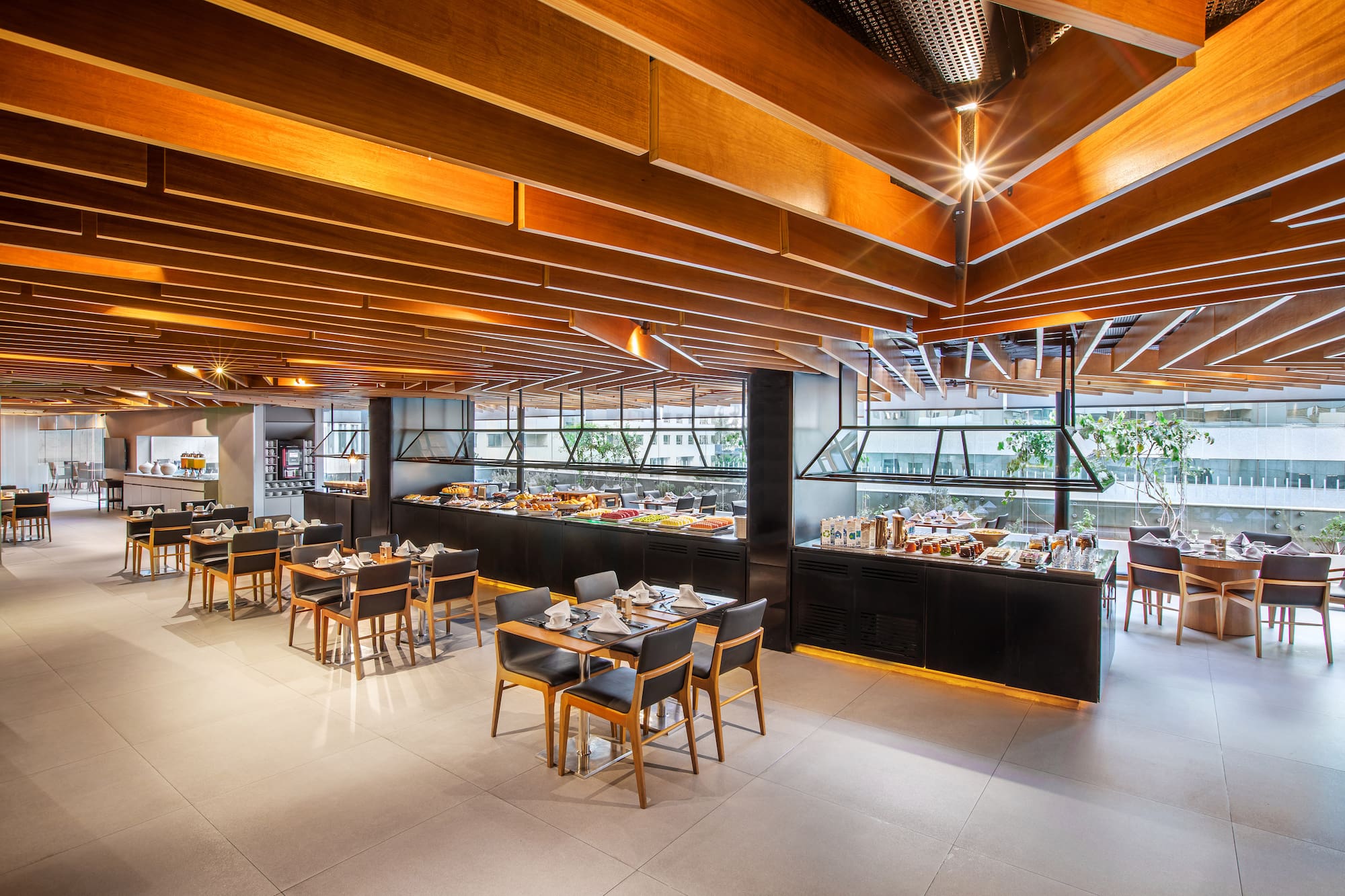 Modern hotel restaurant buffet with food, dining tables, and wood ceiling.