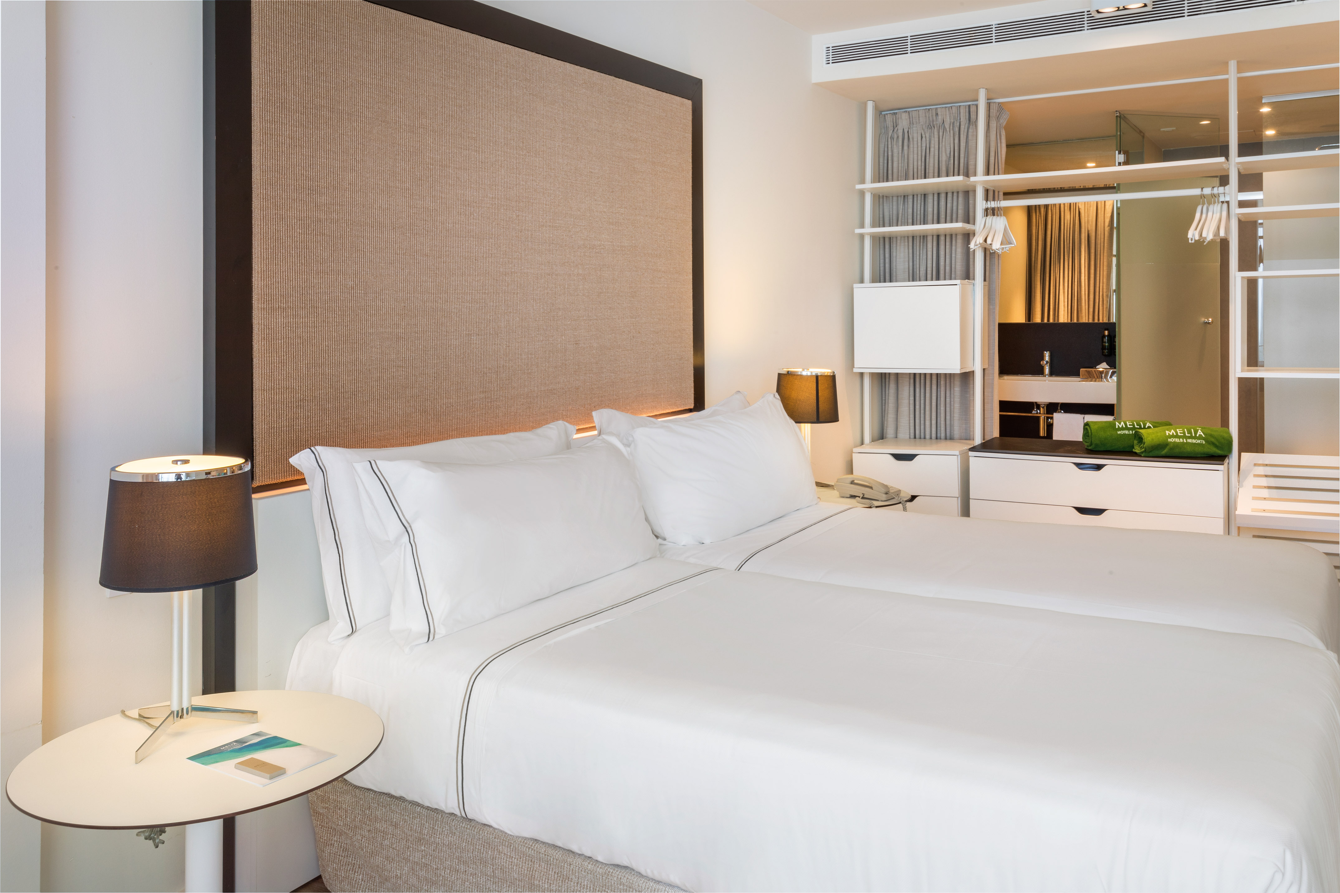 Meliá hotel room with twin beds, white linens, modern design, and storage.