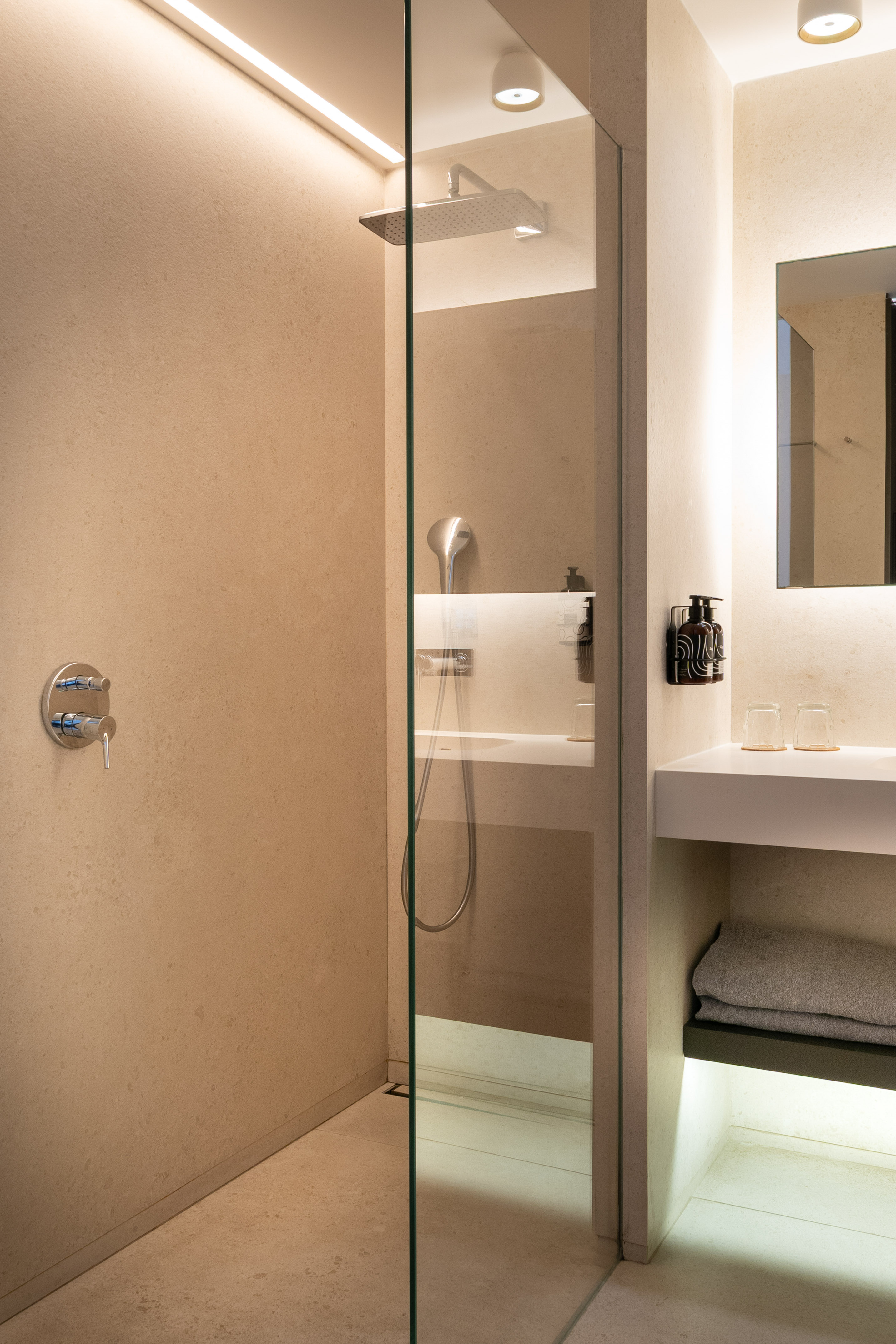 Modern beige bathroom with glass walk-in shower, rain head, and lighted vanity.