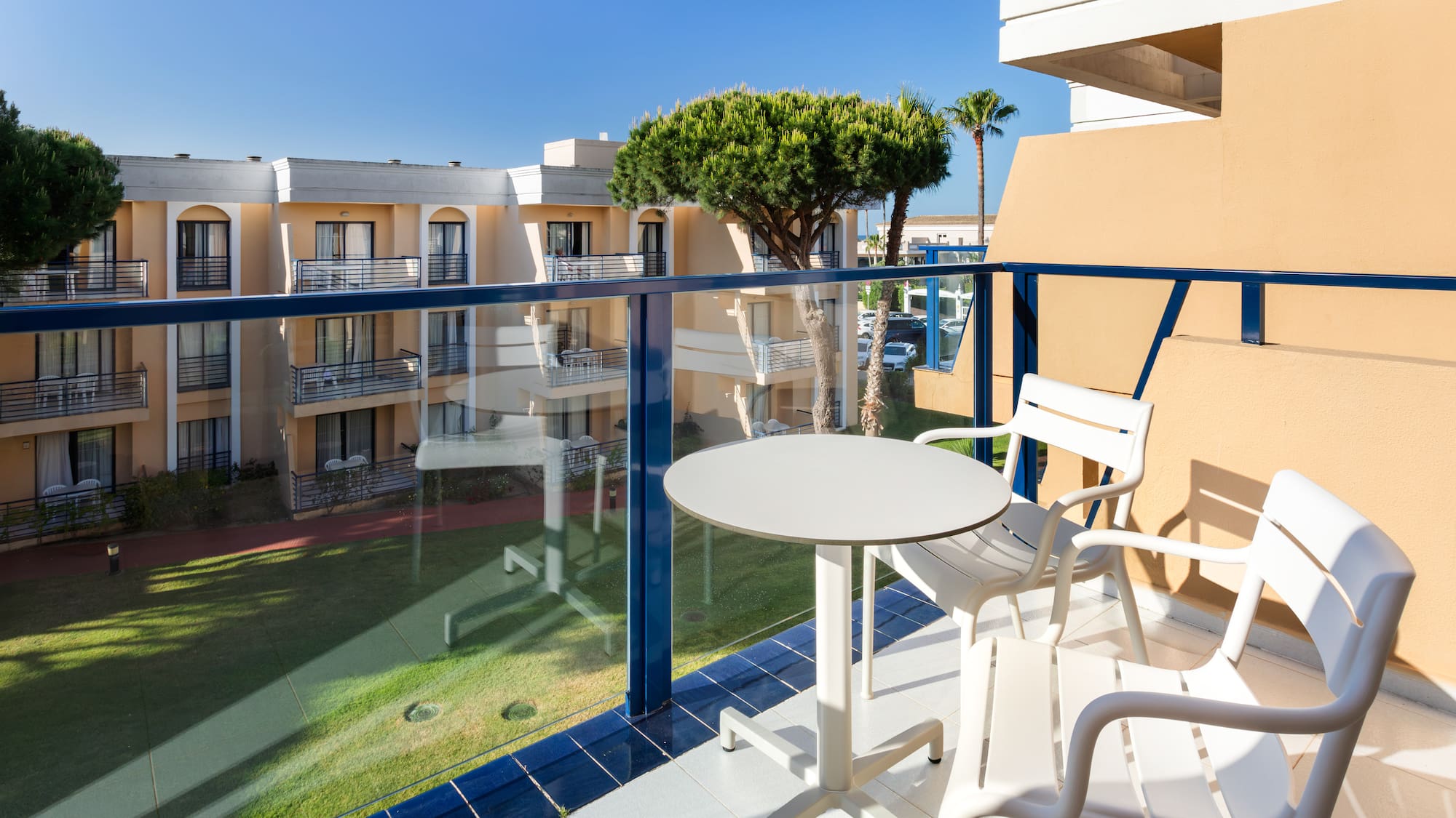 Sunny hotel balcony with white outdoor furniture and garden view.