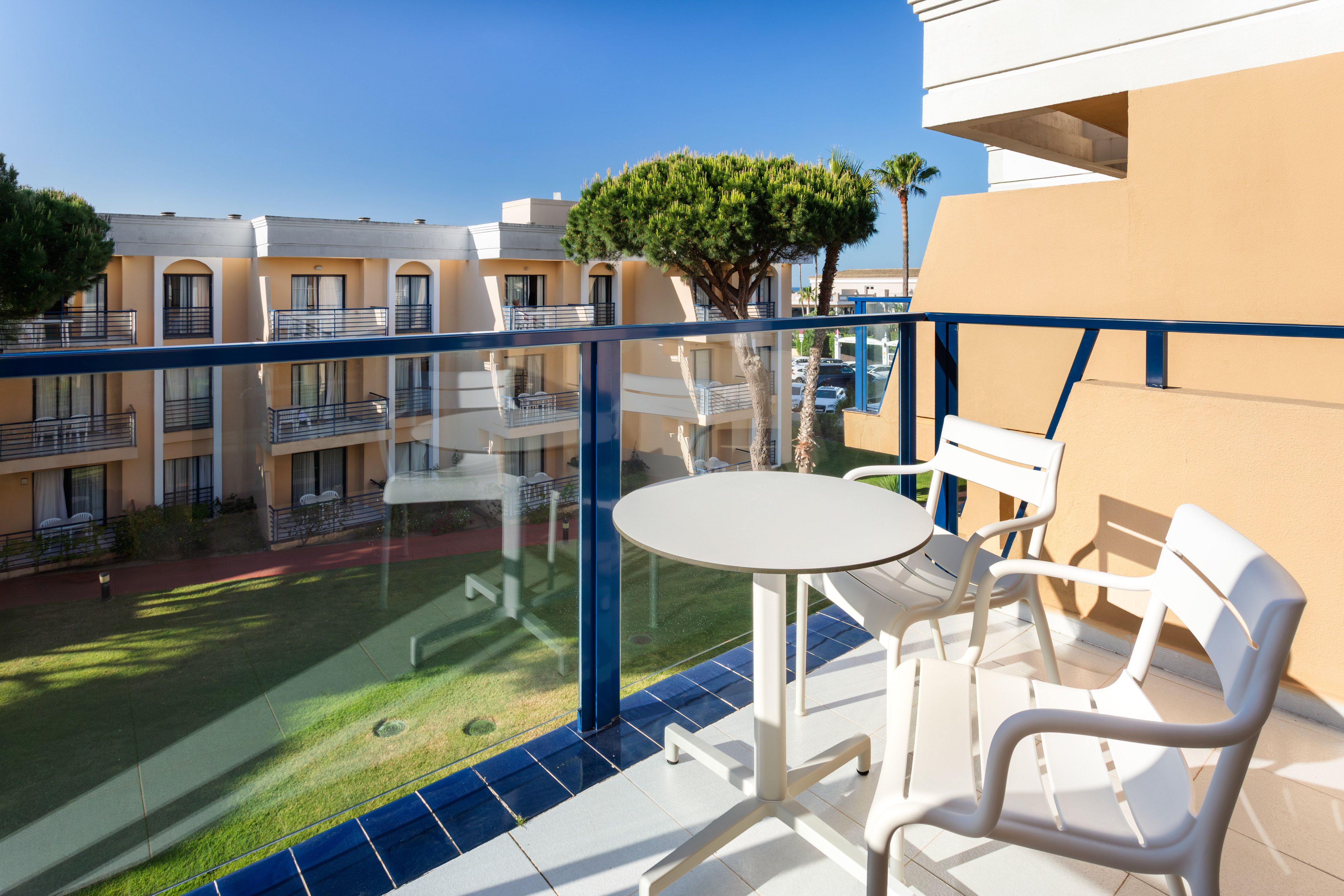 Sunny hotel balcony with white outdoor furniture and garden view.