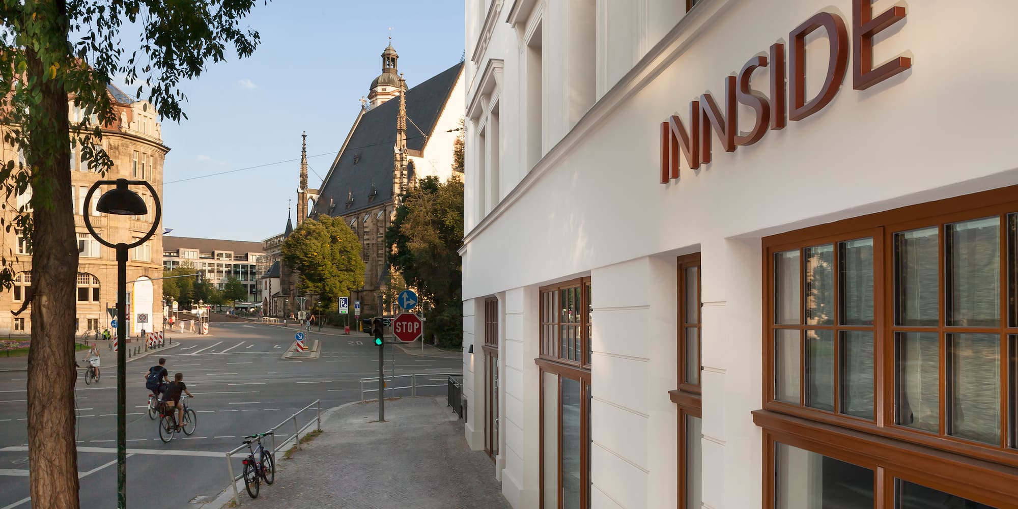 INNSIDE hotel facade, city street with cyclists, and historic church.
