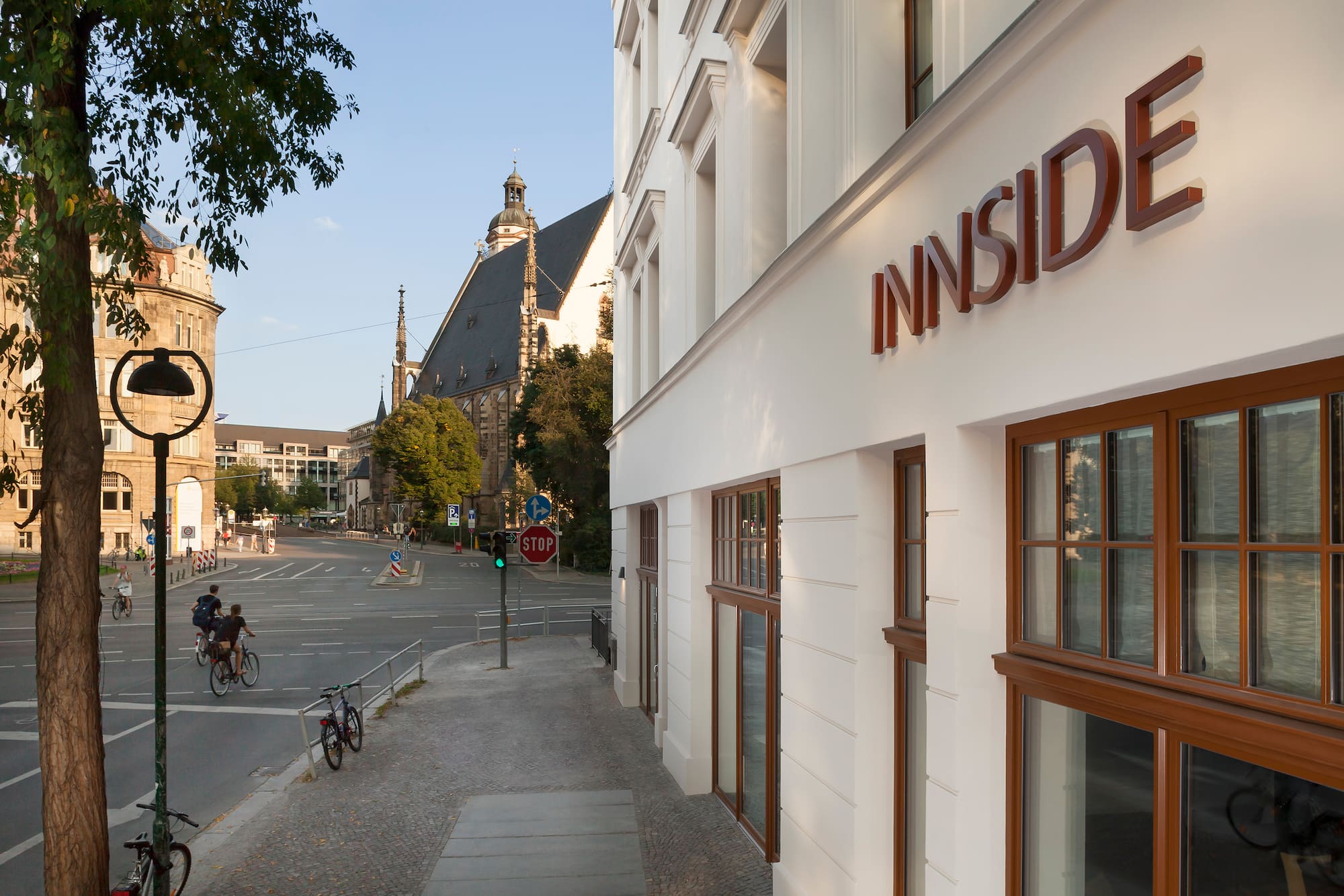 INNSIDE hotel building and St. Nicholas Church, Leipzig city street with cyclists.