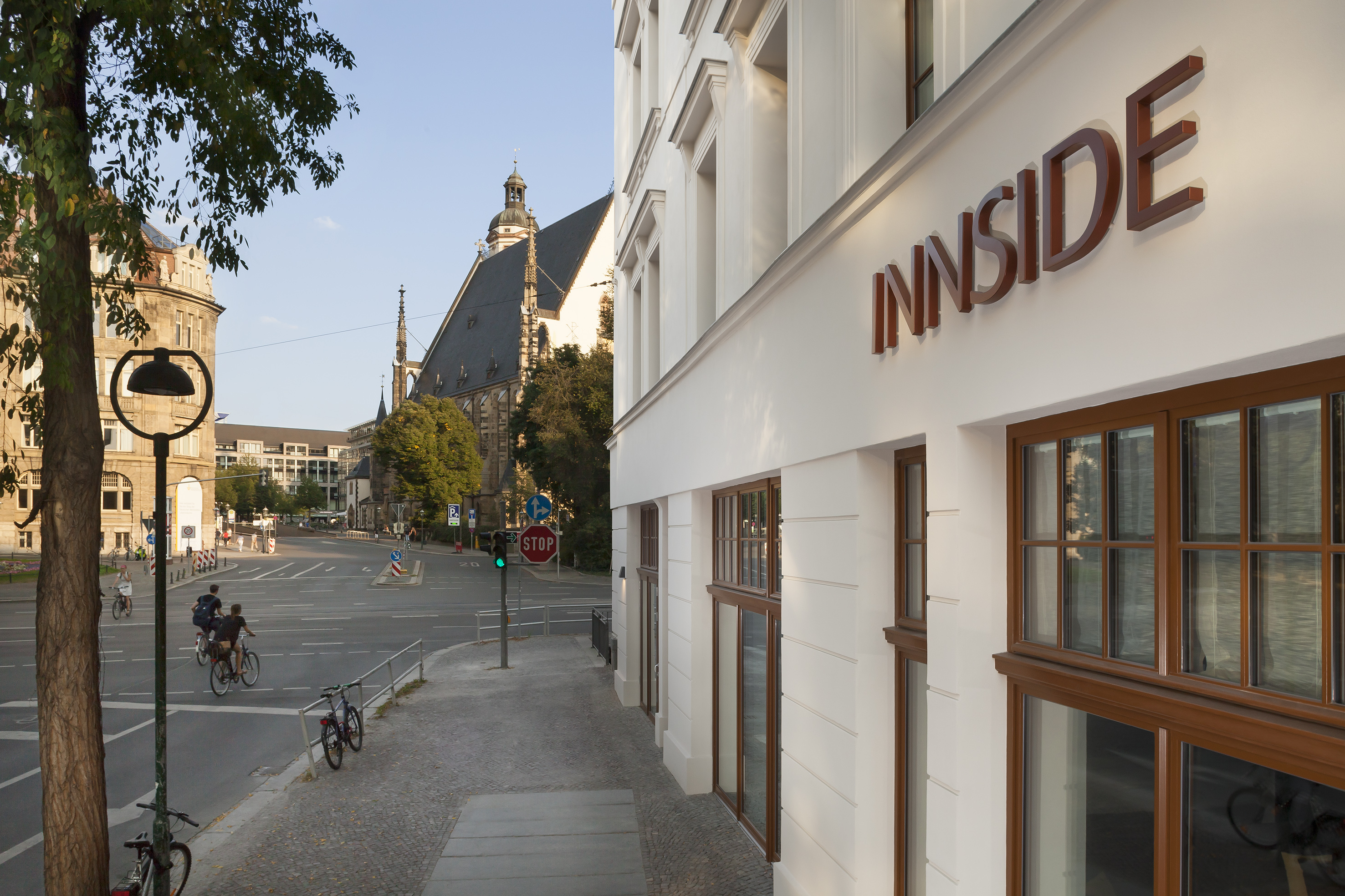 INNSIDE hotel facade, city street with cyclists, and historic church.
