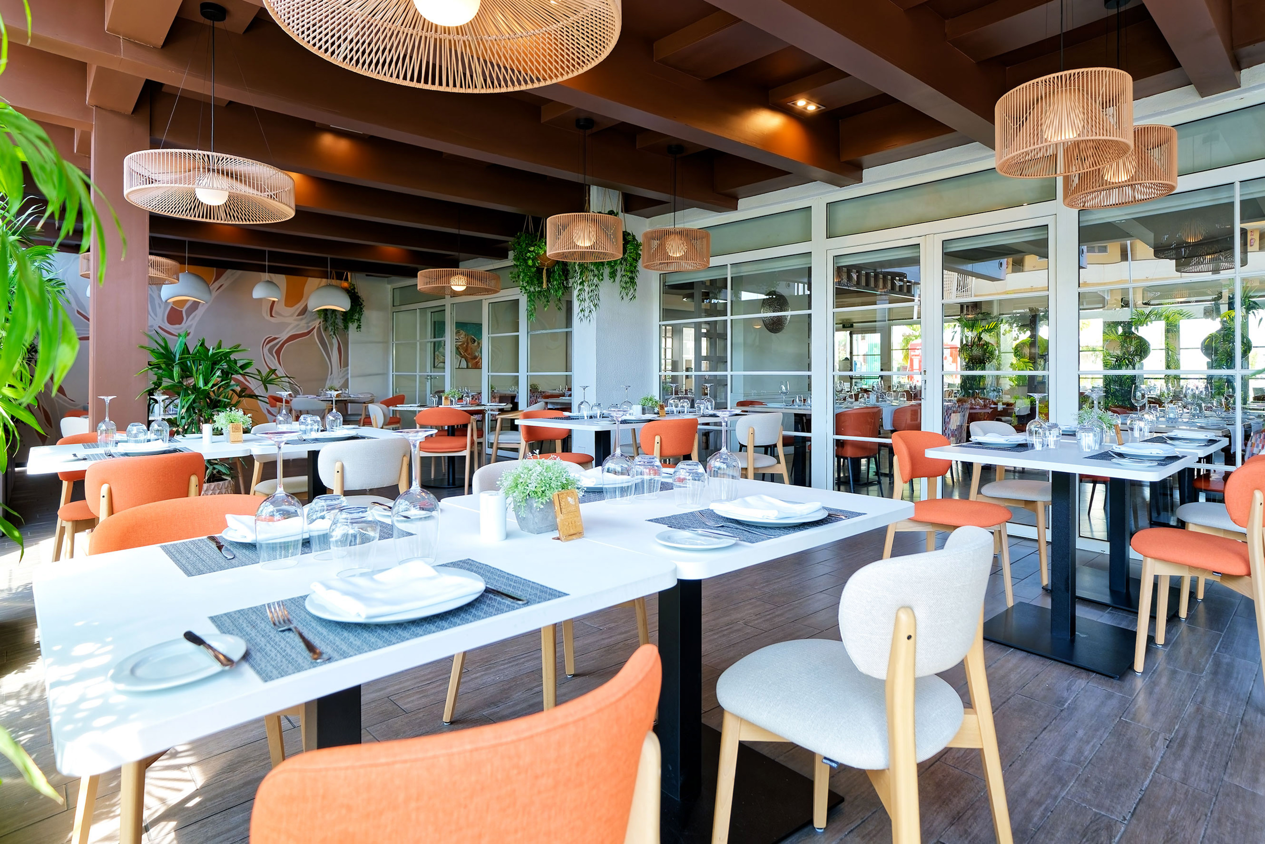 Bright, modern restaurant dining area with orange chairs, white tables, and wicker lights.