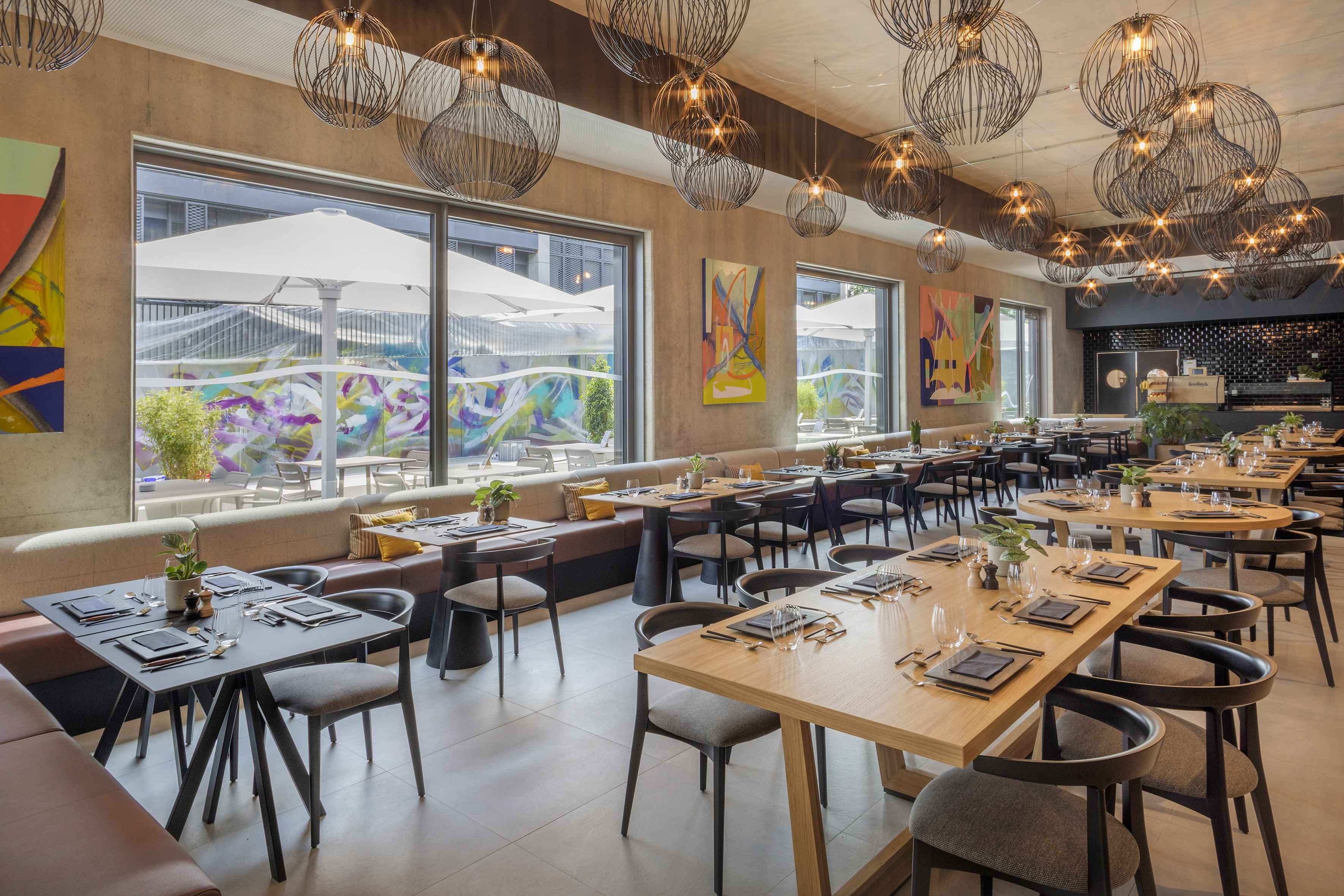 Modern restaurant interior with set tables, pendant lights, and vibrant patio view.