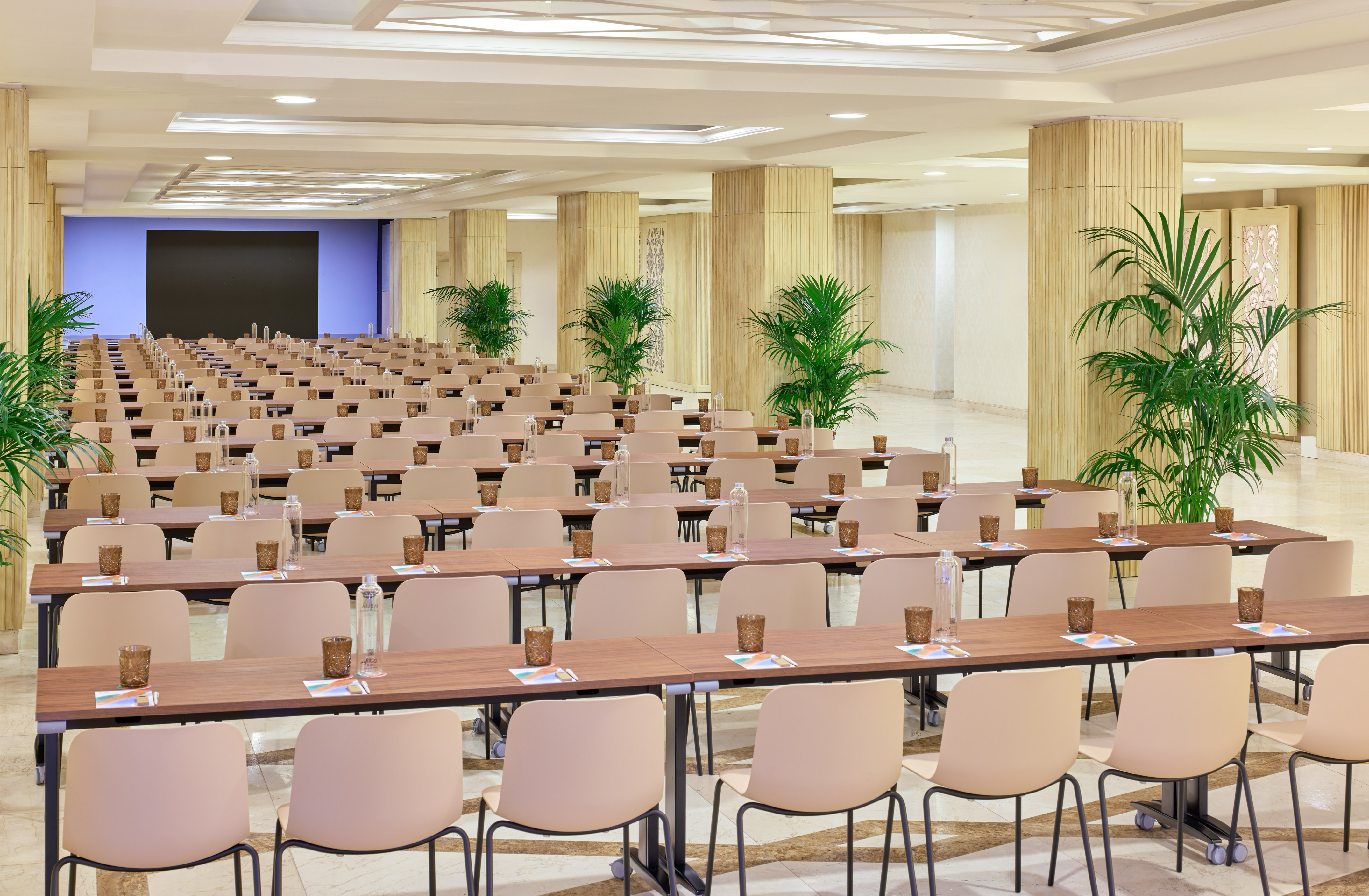 Conference room with classroom setup, tables, chairs, screen, and plants.