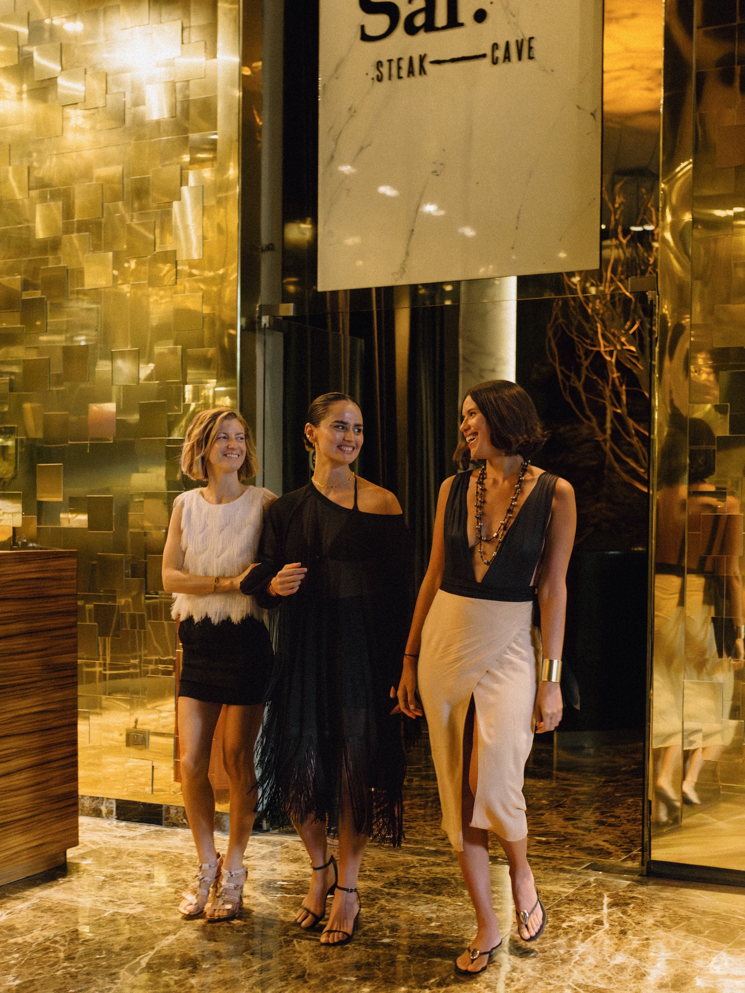 Three women smiling, entering Sal. Steak — Cave luxury restaurant.