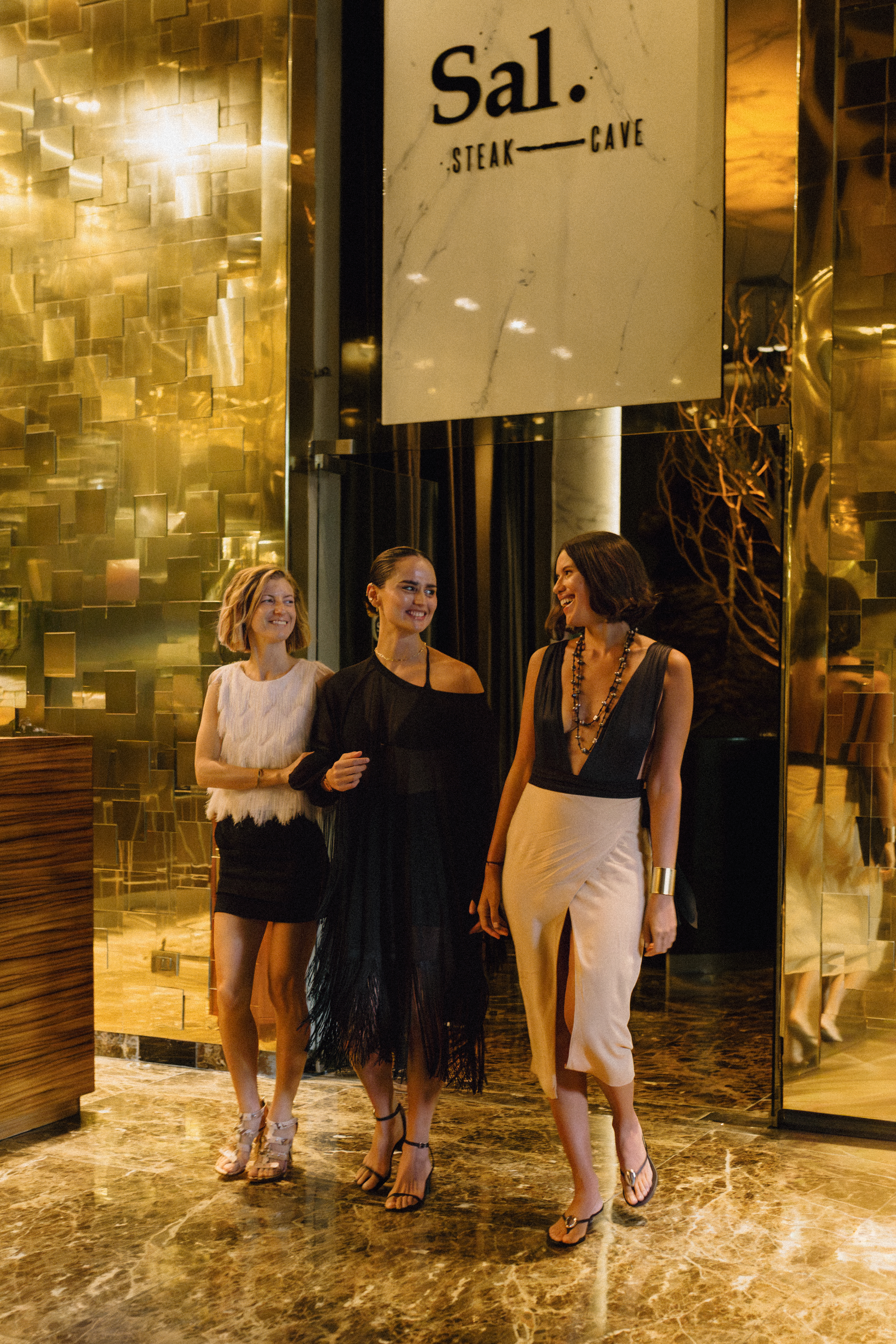 Three women smiling, entering Sal. Steak — Cave luxury restaurant.