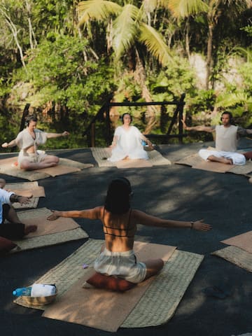 a group of people sitting on mats in a circle with trees in the background